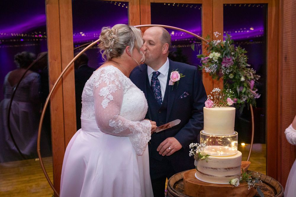 Bride and groom sharing a kiss while cutting their elegant three-tier wedding cake at their reception.