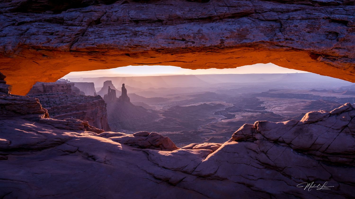 Natural stone arch frames distant desert spires in misty morning light.