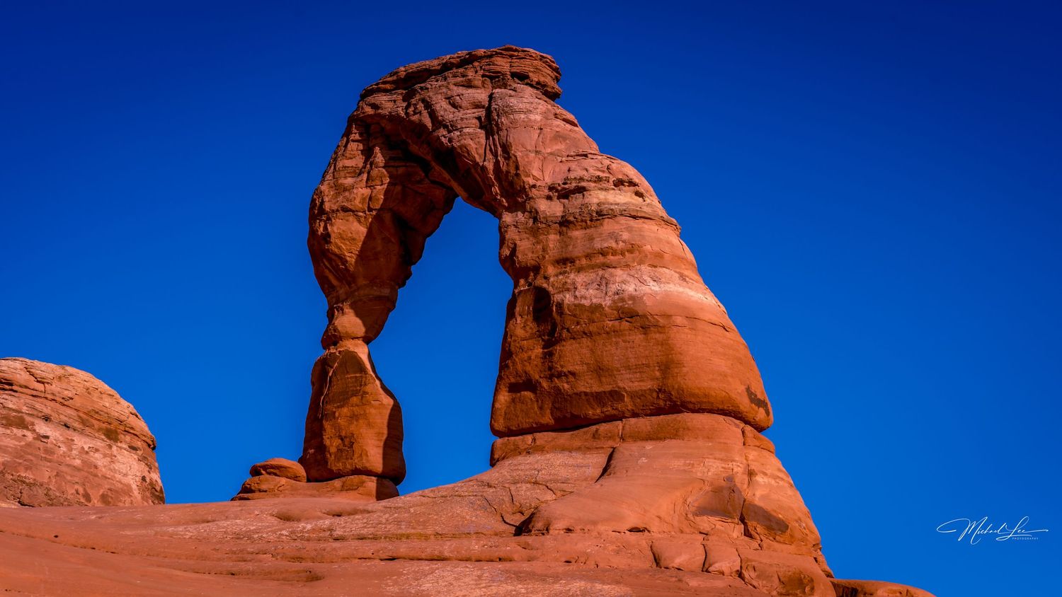 Delicate Arch stands majestically against bright blue sky in Utah's desert landscape.