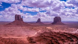 Majestic red rock formations tower over Monument Valley's desert landscape under dramatic cloudy skies.