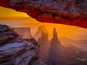 Mesa Arch frames stunning desert canyon vista at sunrise in golden light.
