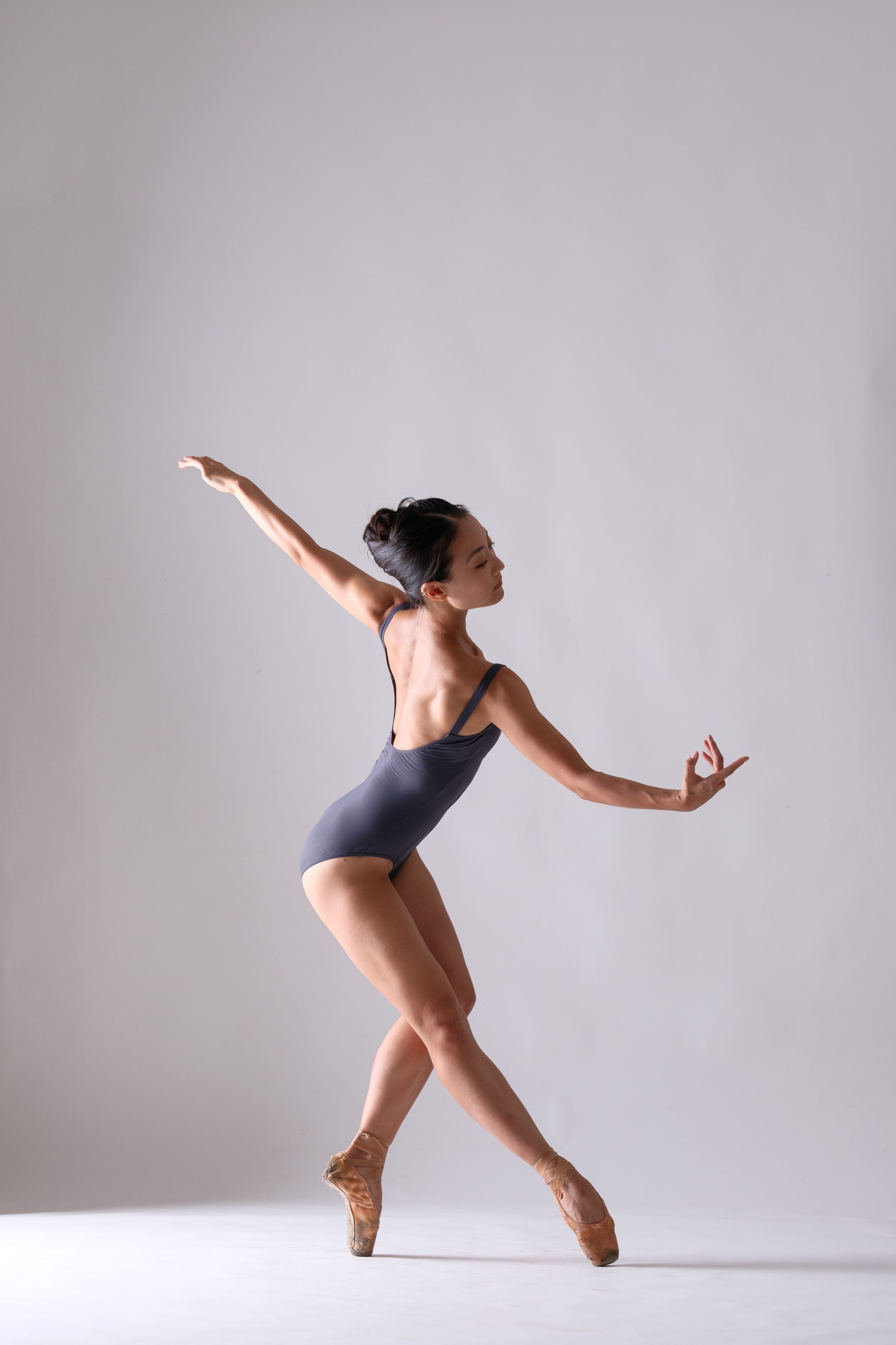 Ballet dancer in navy leotard performs dynamic movement sequence against white backdrop.