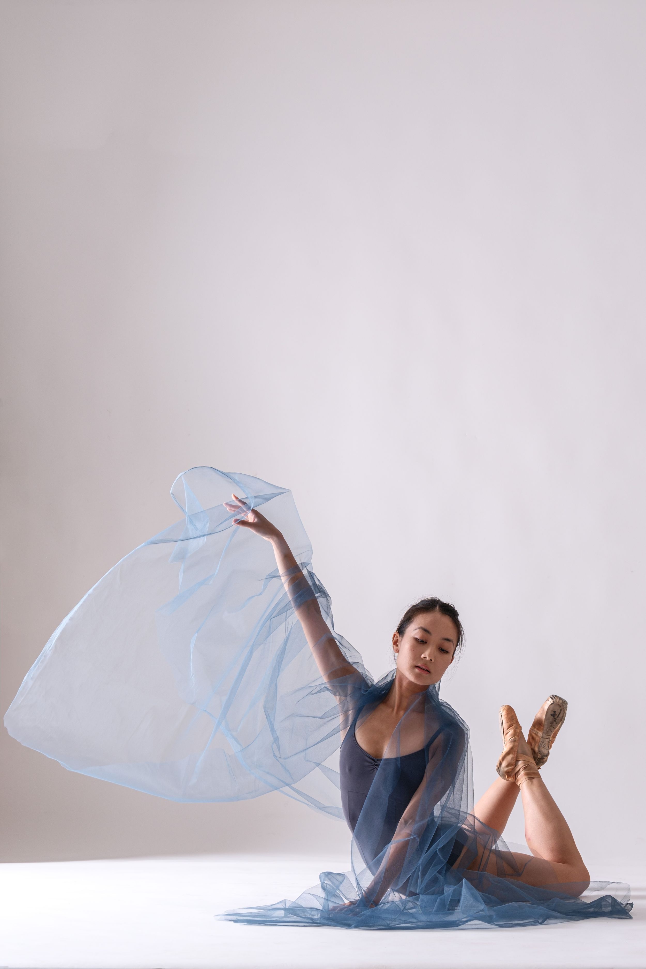 Contemporary dancer performs fluid movements with flowing light blue fabric in minimalist studio.