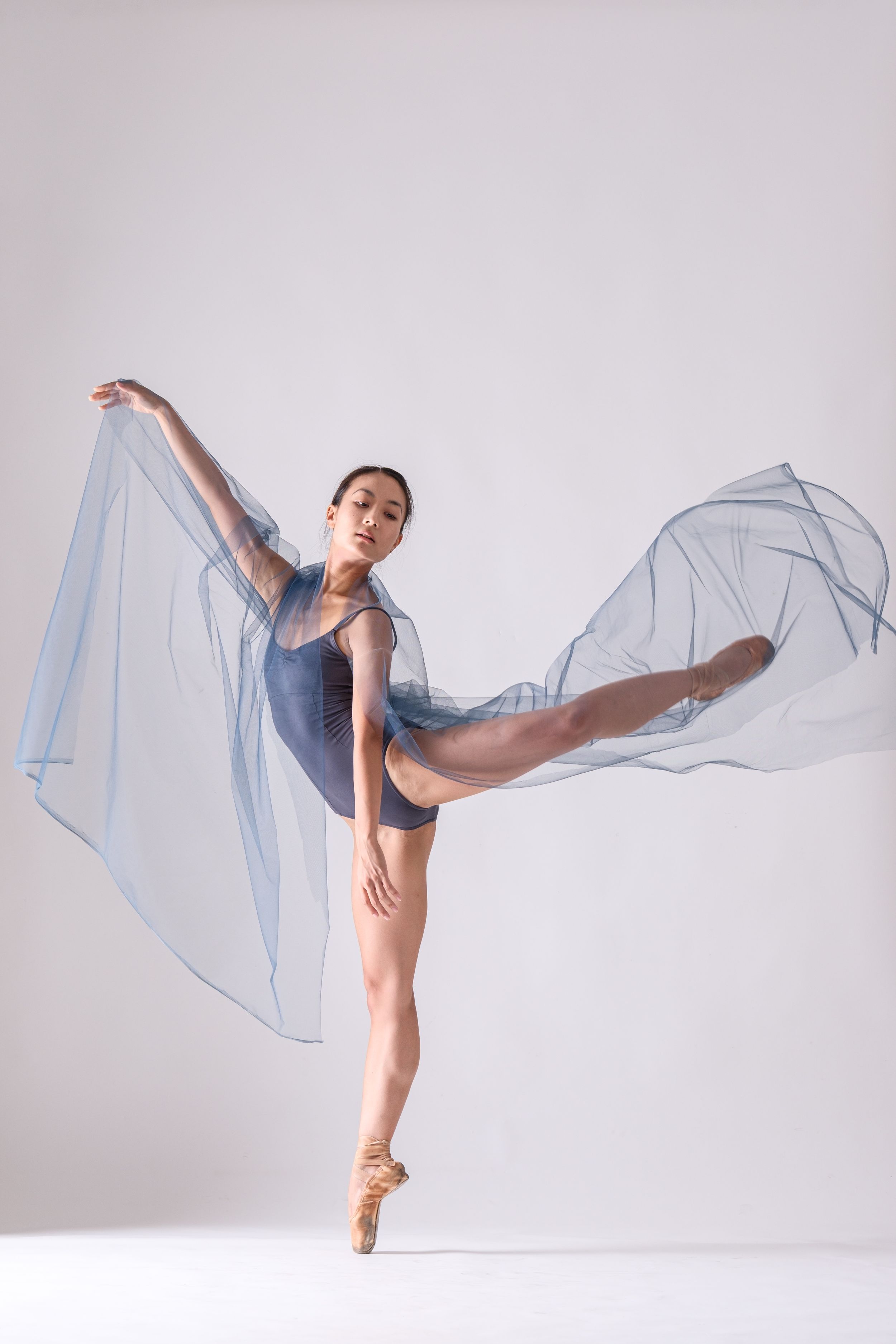 Dancer in blue leotard creates elegant lines with flowing fabric in studio setting.
