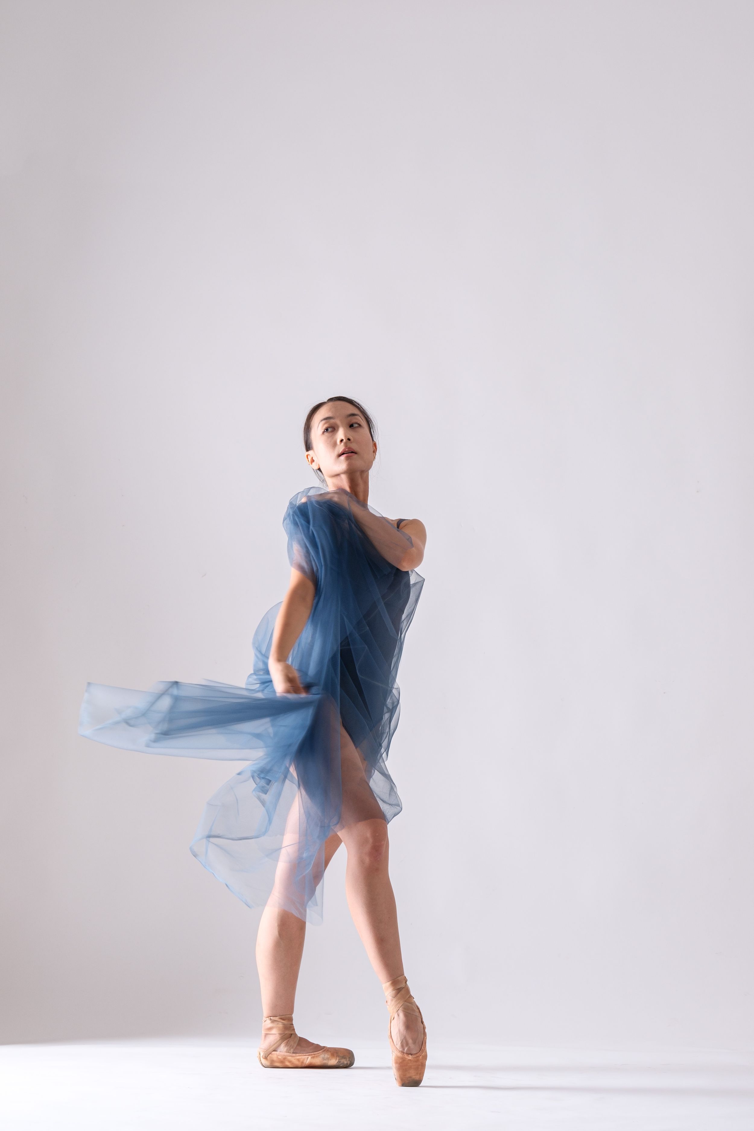 Dancer creates dramatic pose with sheer blue fabric against stark white background.