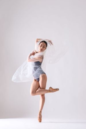 Ballet dancer performs graceful movements in white flowing fabric against light background.