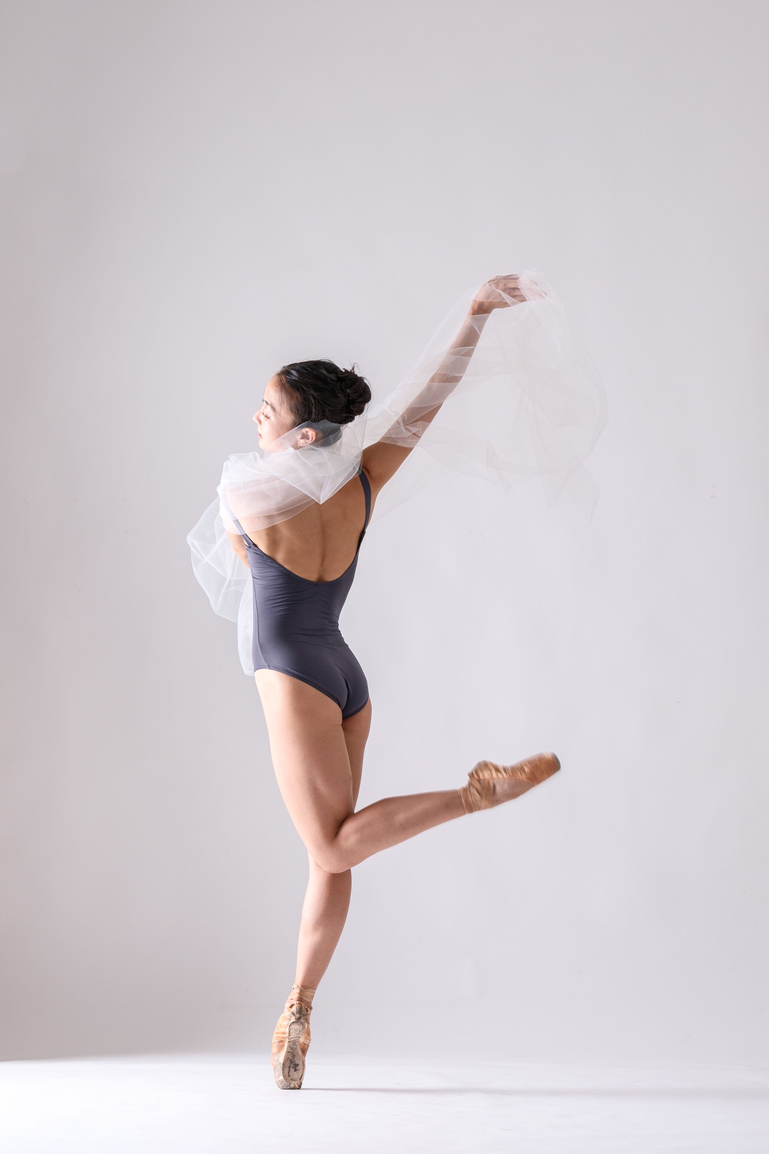Dancer demonstrates elegant ballet positions in grey leotard against white background.