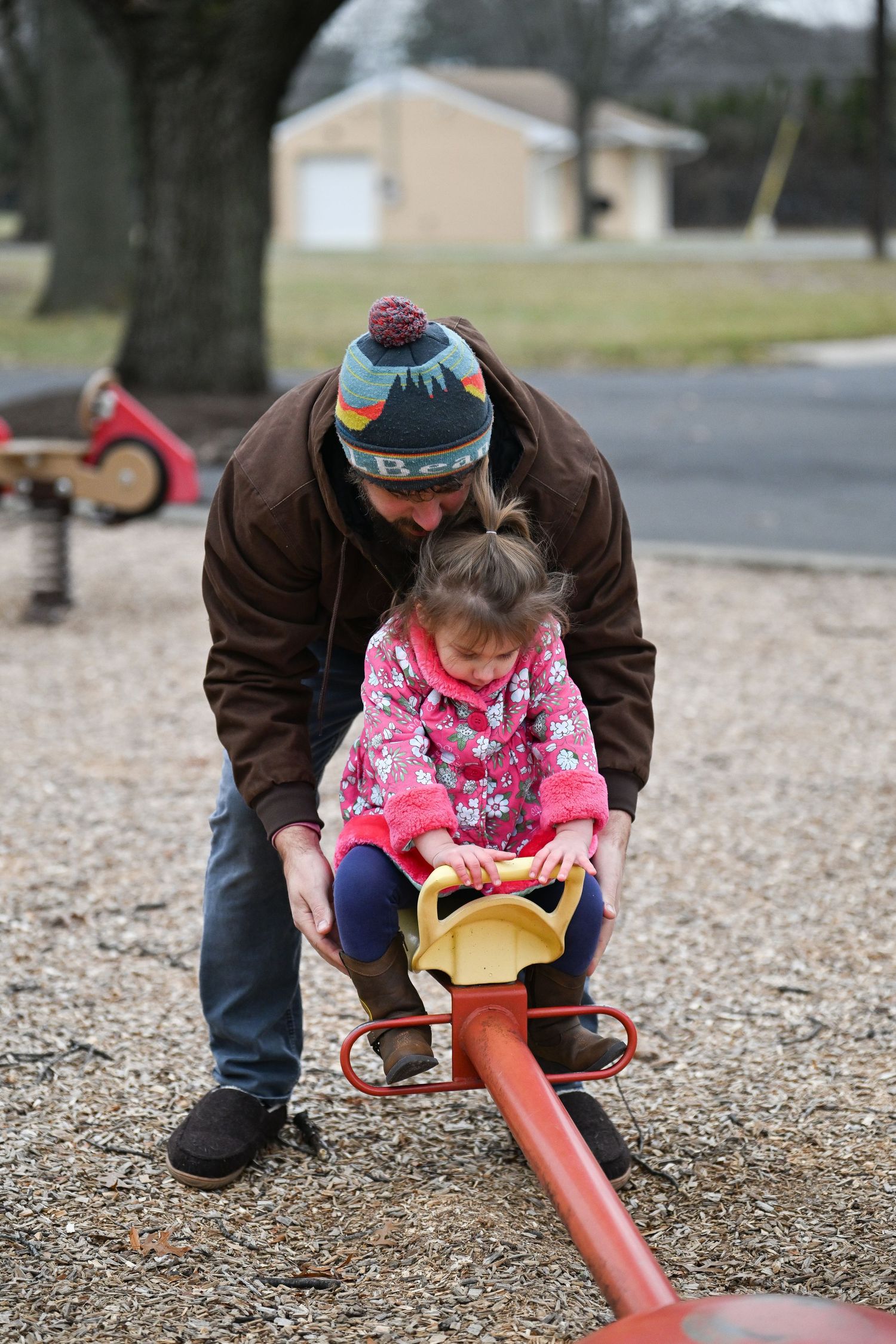 A photograph of Evan helping his young daughter Emma use the see-saws at the park