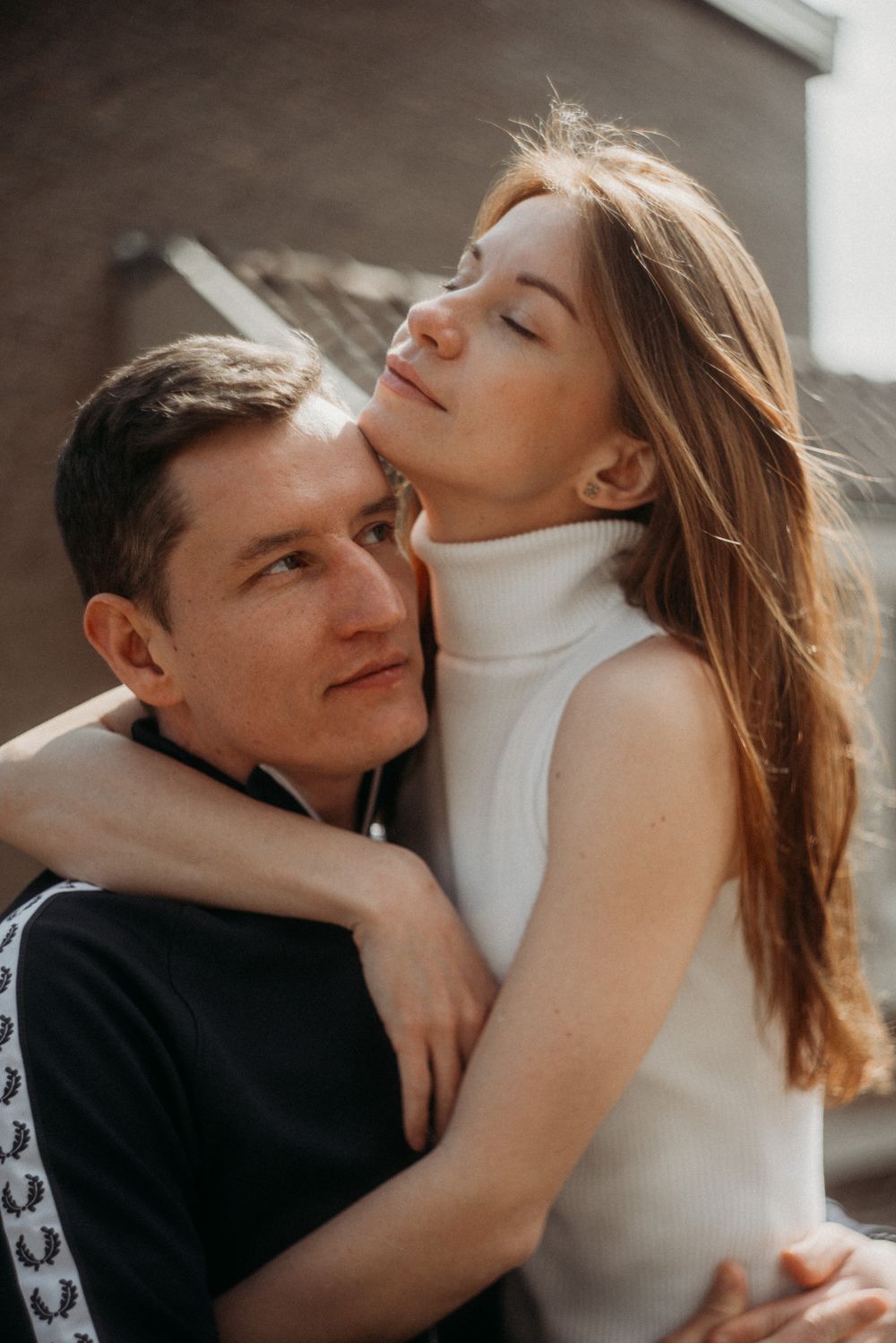 Intimate couple embracing in romantic natural lighting by window.