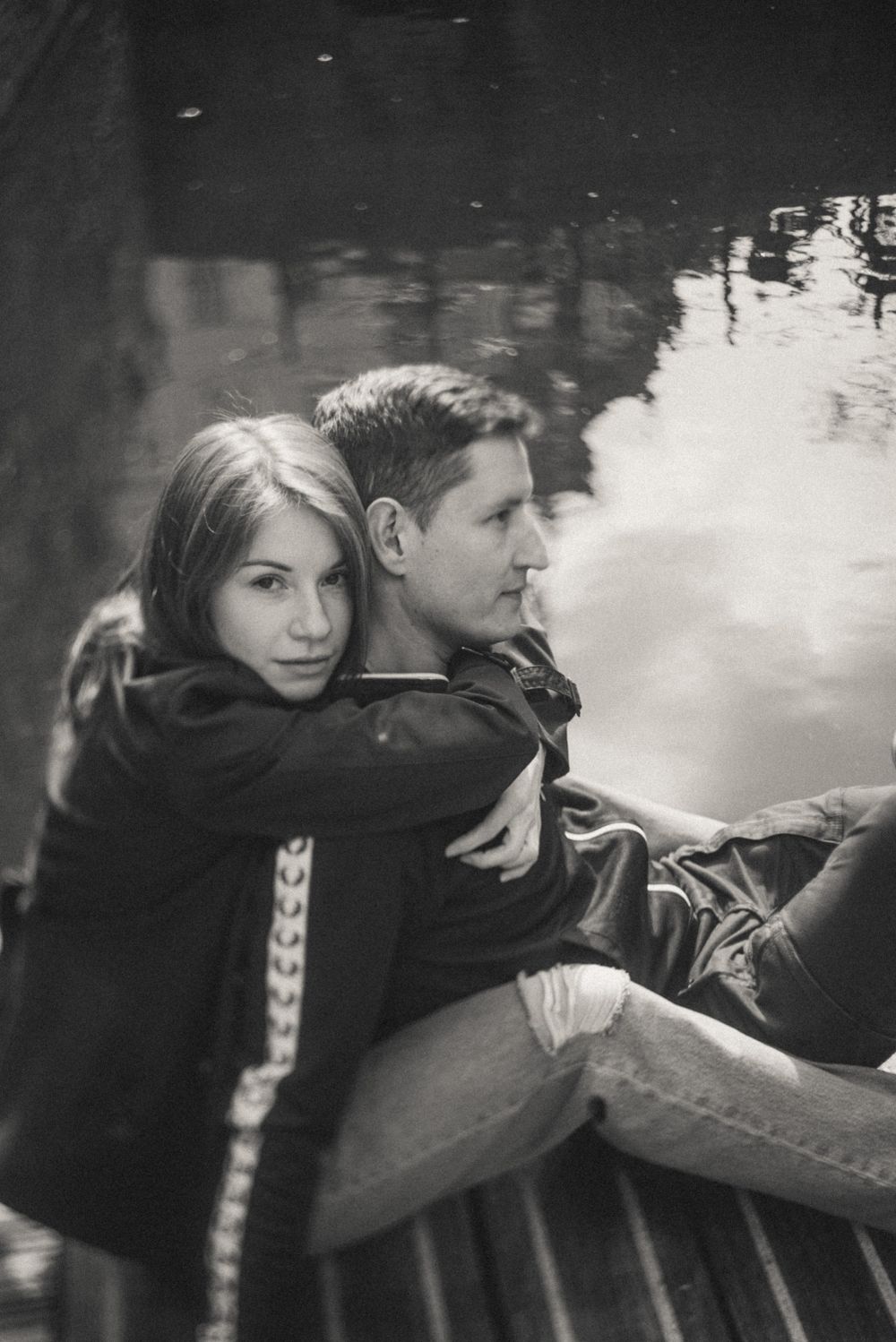 A couple embraces by a reflective pond in atmospheric black and white photography.