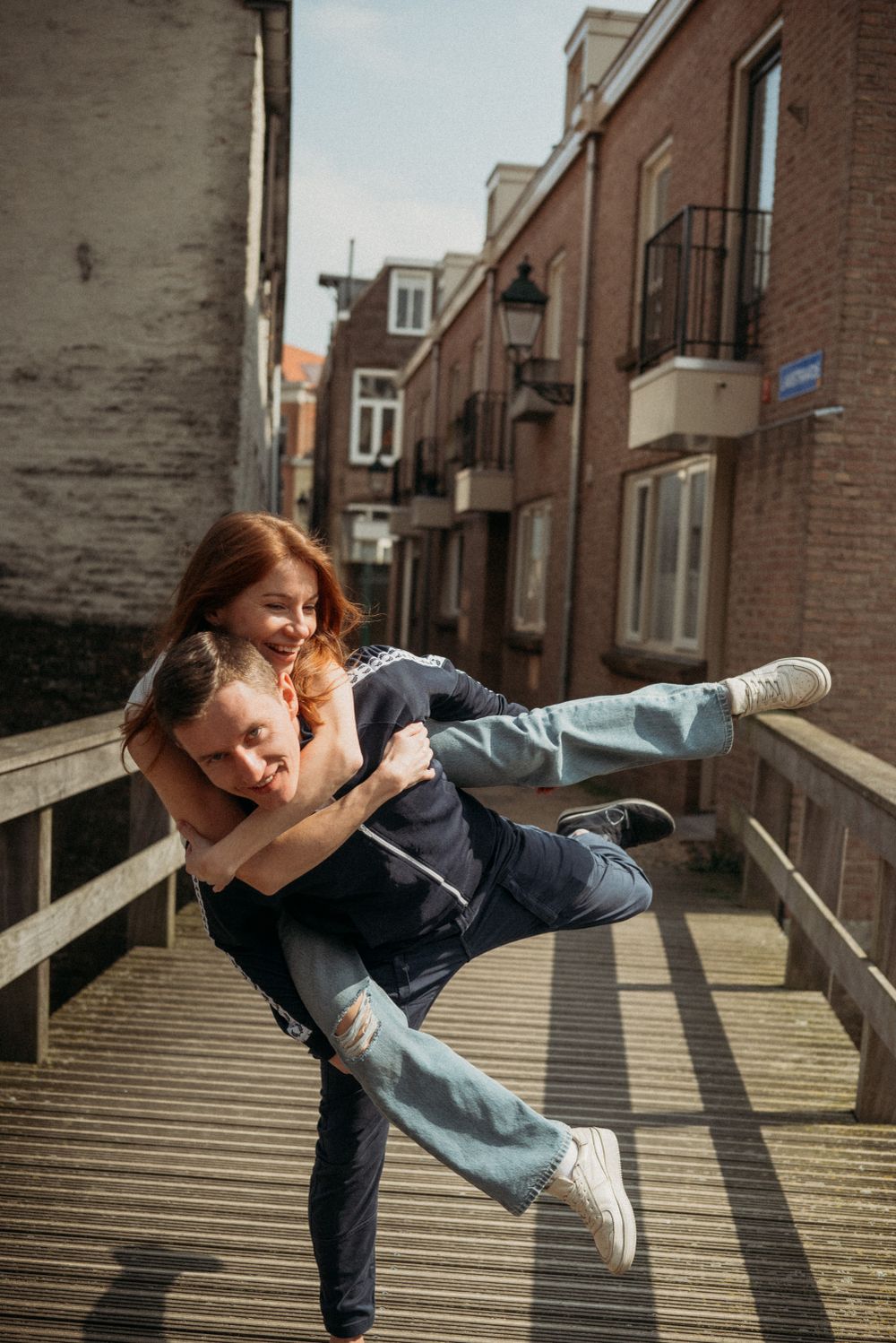 A couple poses playfully on wooden steps in an urban setting with brick buildings.