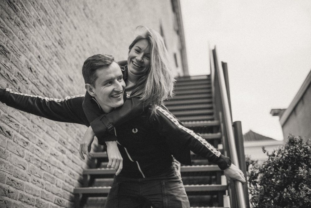 A couple laughs and embraces in black and white against a brick wall backdrop.