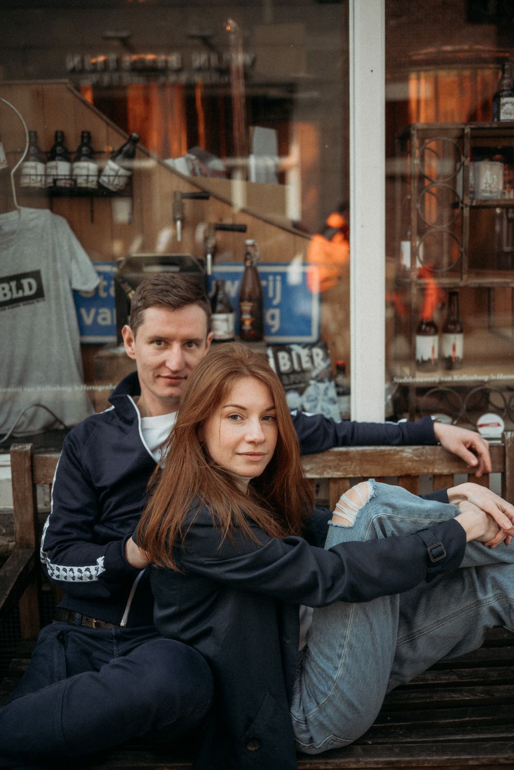 A couple poses intimately in front of a vintage storefront window.