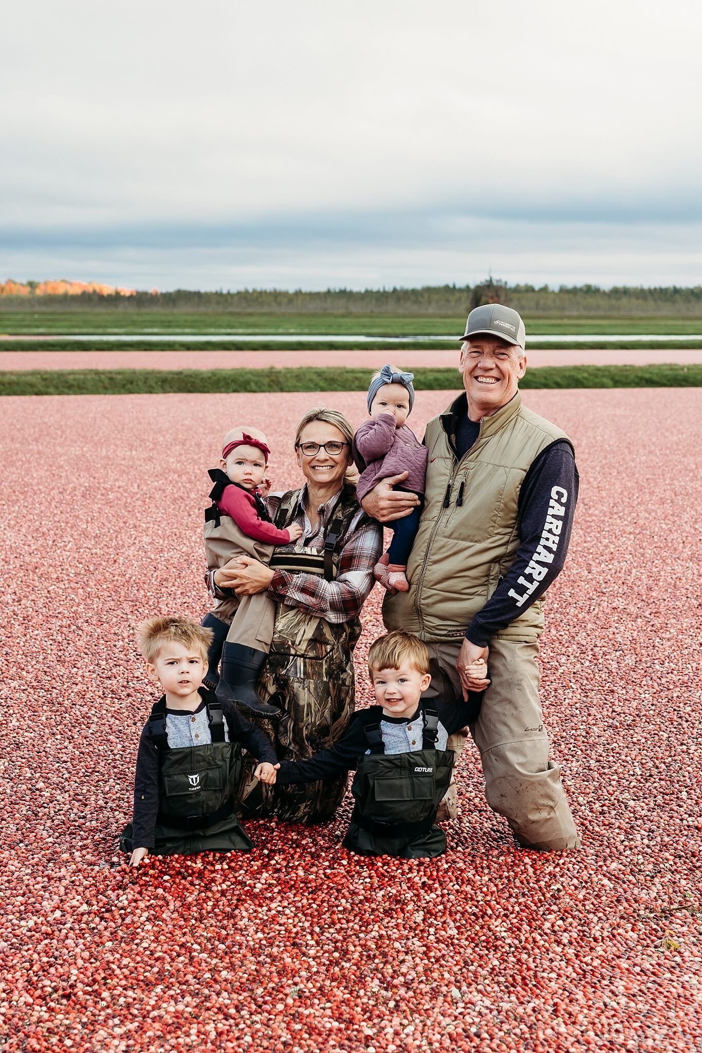 A family of six poses in a bright red cranberry bog during harvest time.