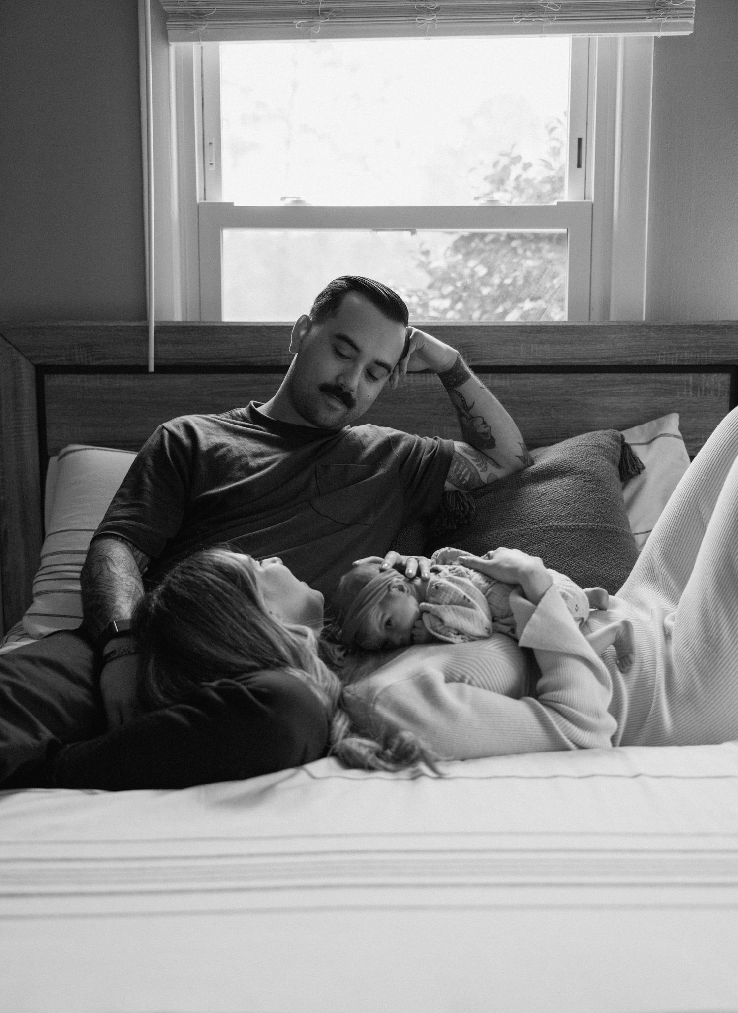 A black and white photograph showing a quiet moment of rest on a couch by a window with natural light streaming in.