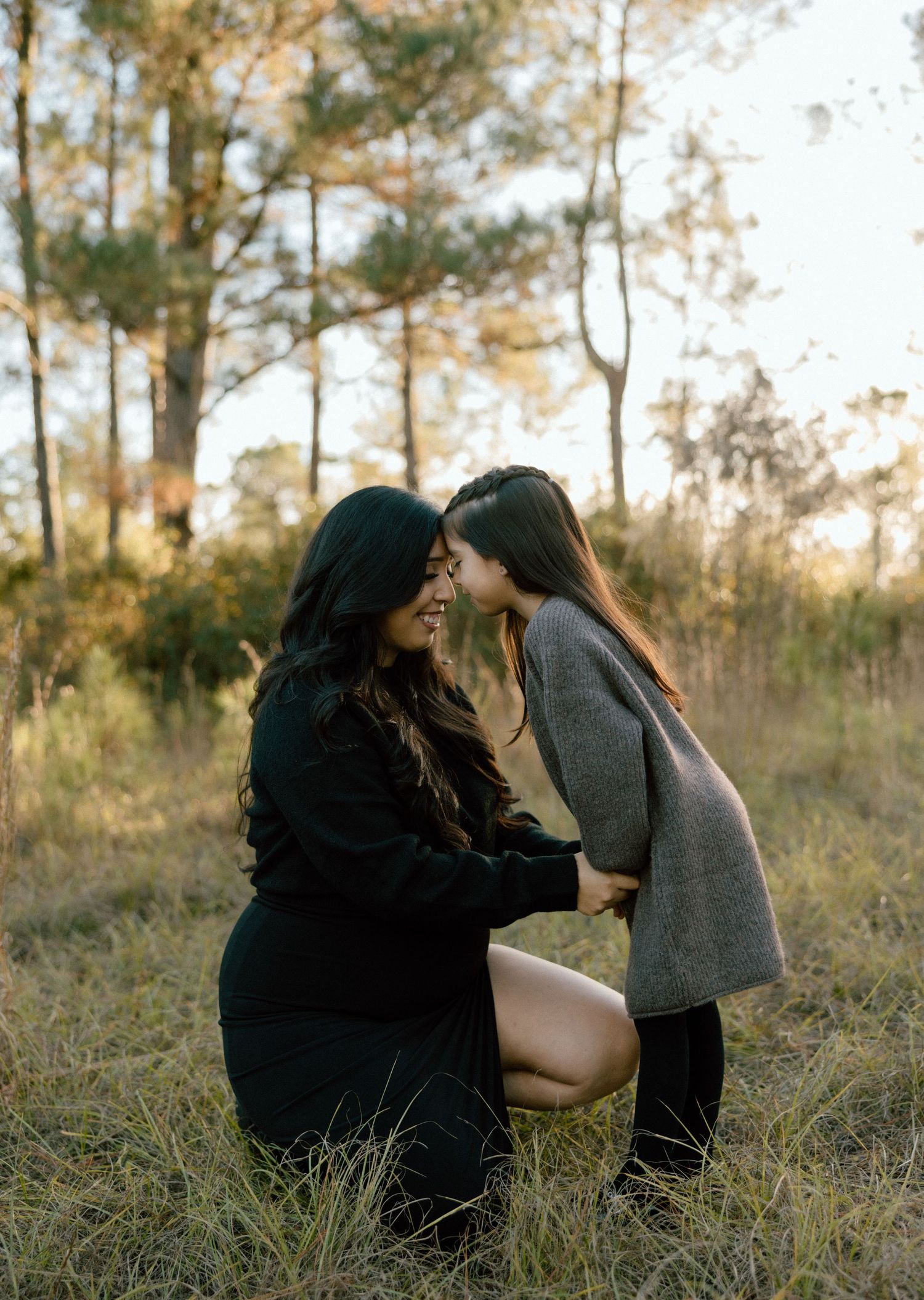 a mother and a daughter sharing an intimate moment outdoors in a wooded area during golden hour.