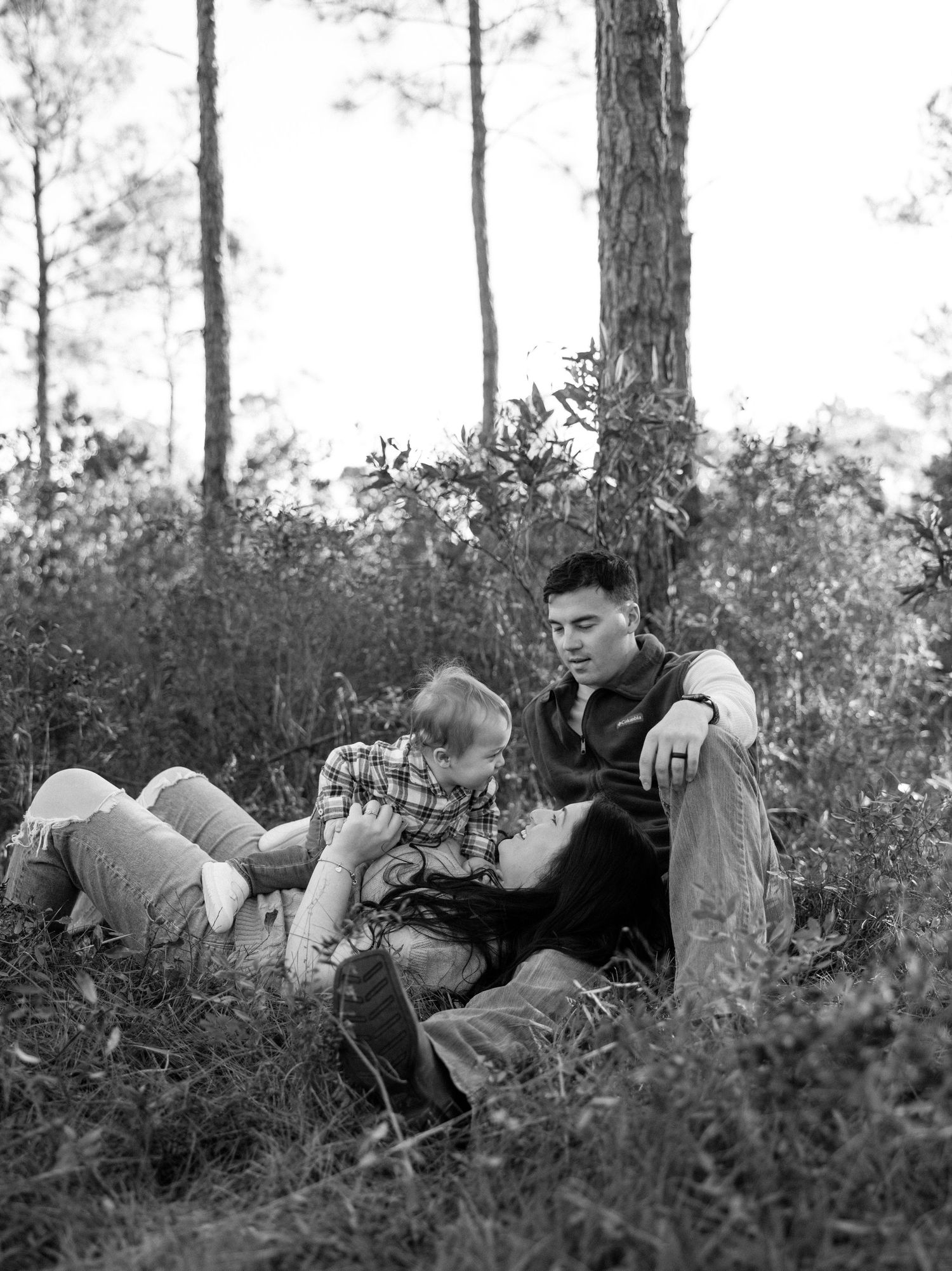 Soldiers in combat gear lie prone on the ground among brush and trees during a military training exercise.