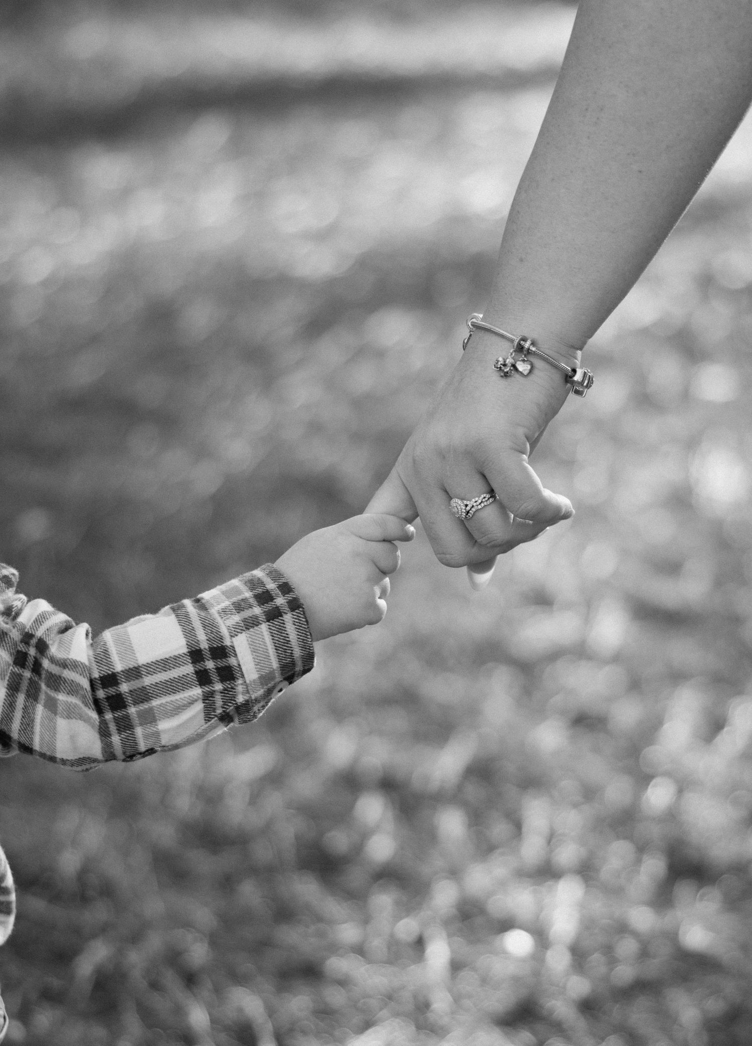 Two hands holding each other in a loving gesture, photographed in black and white with a blurred background.