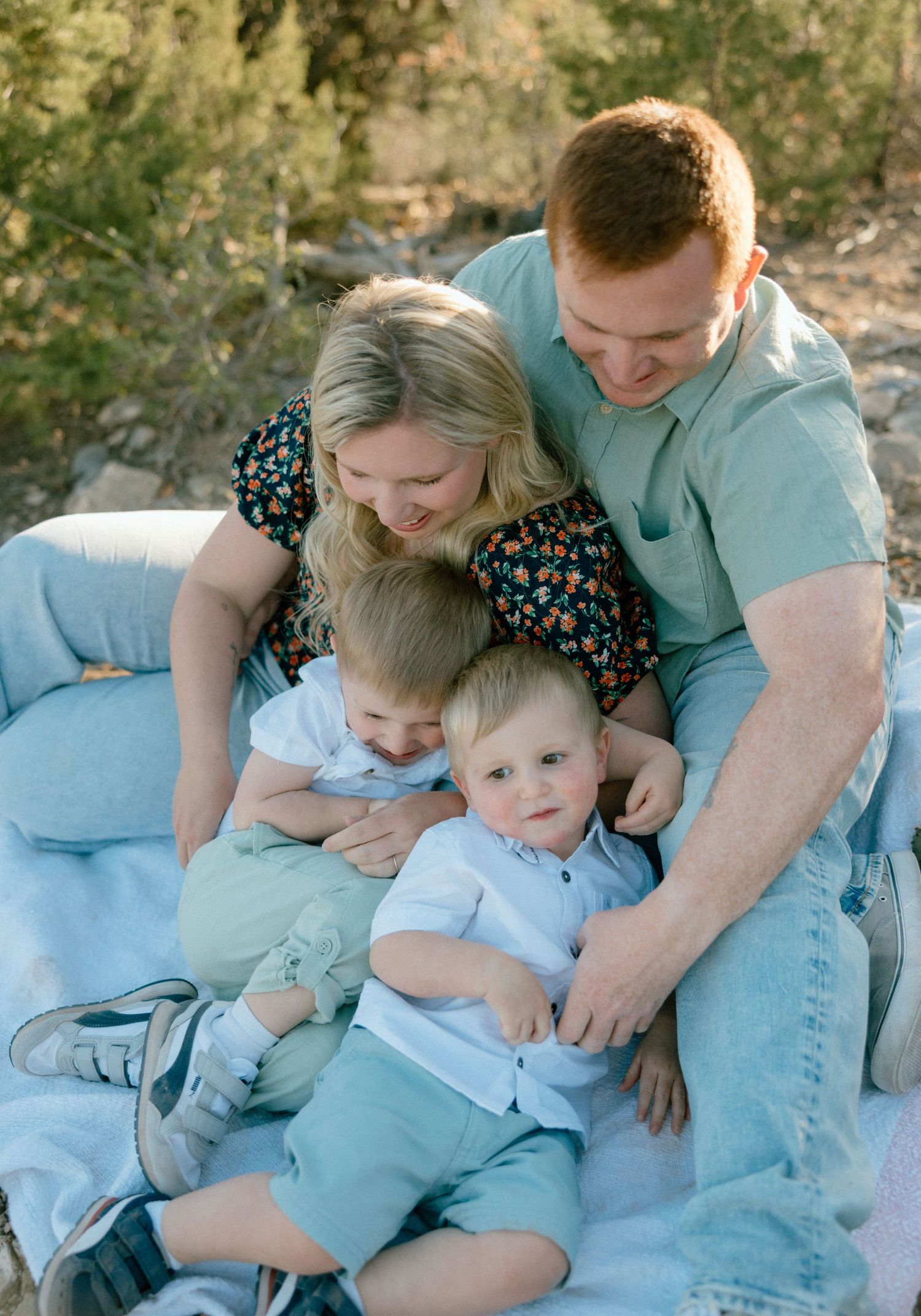 Family snuggling together on a light blue blanket outdoors in a series of candid moments.
