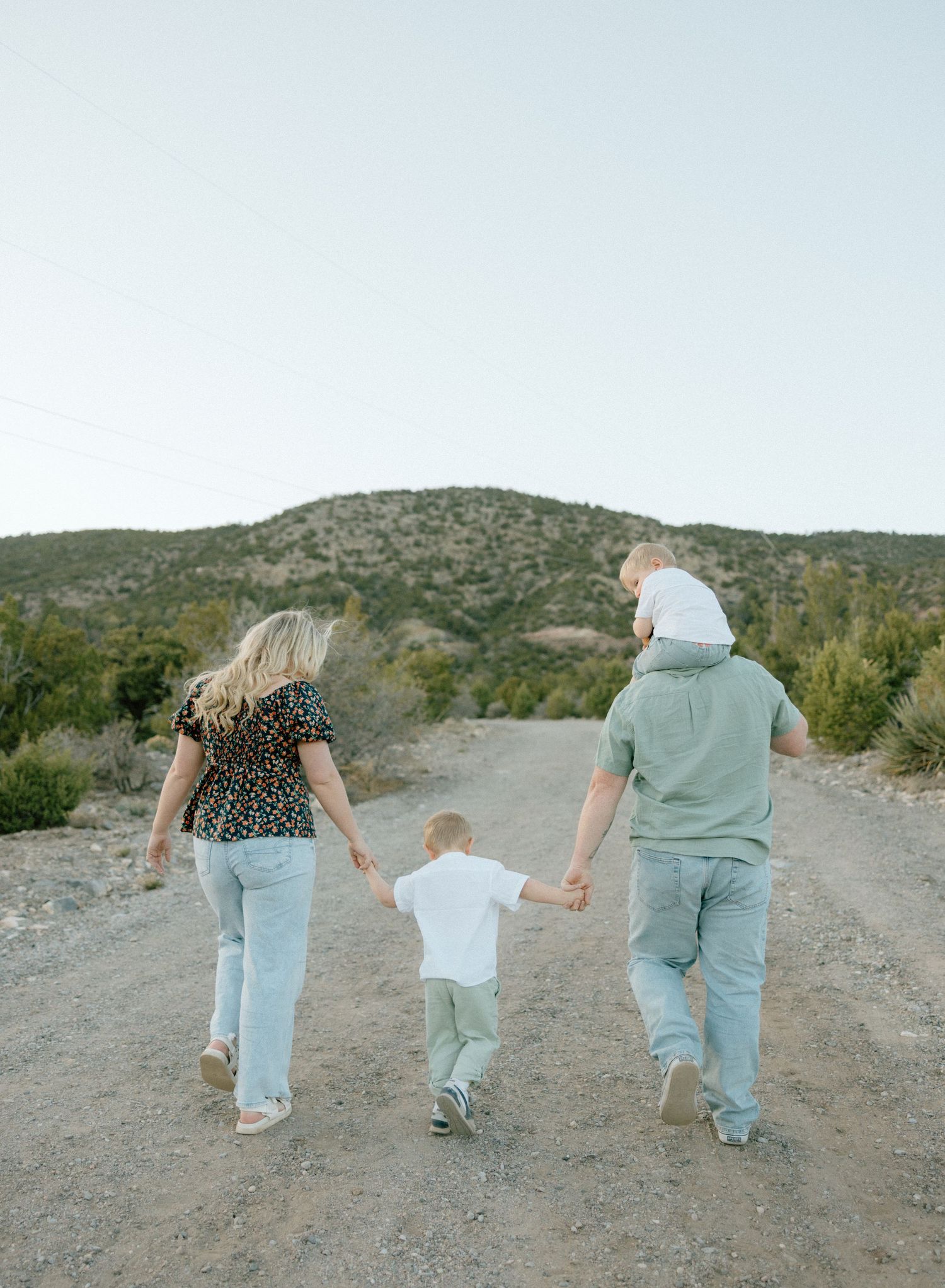 A family walking hand in hand along a dusty desert trail at sunset with mountains in the background.