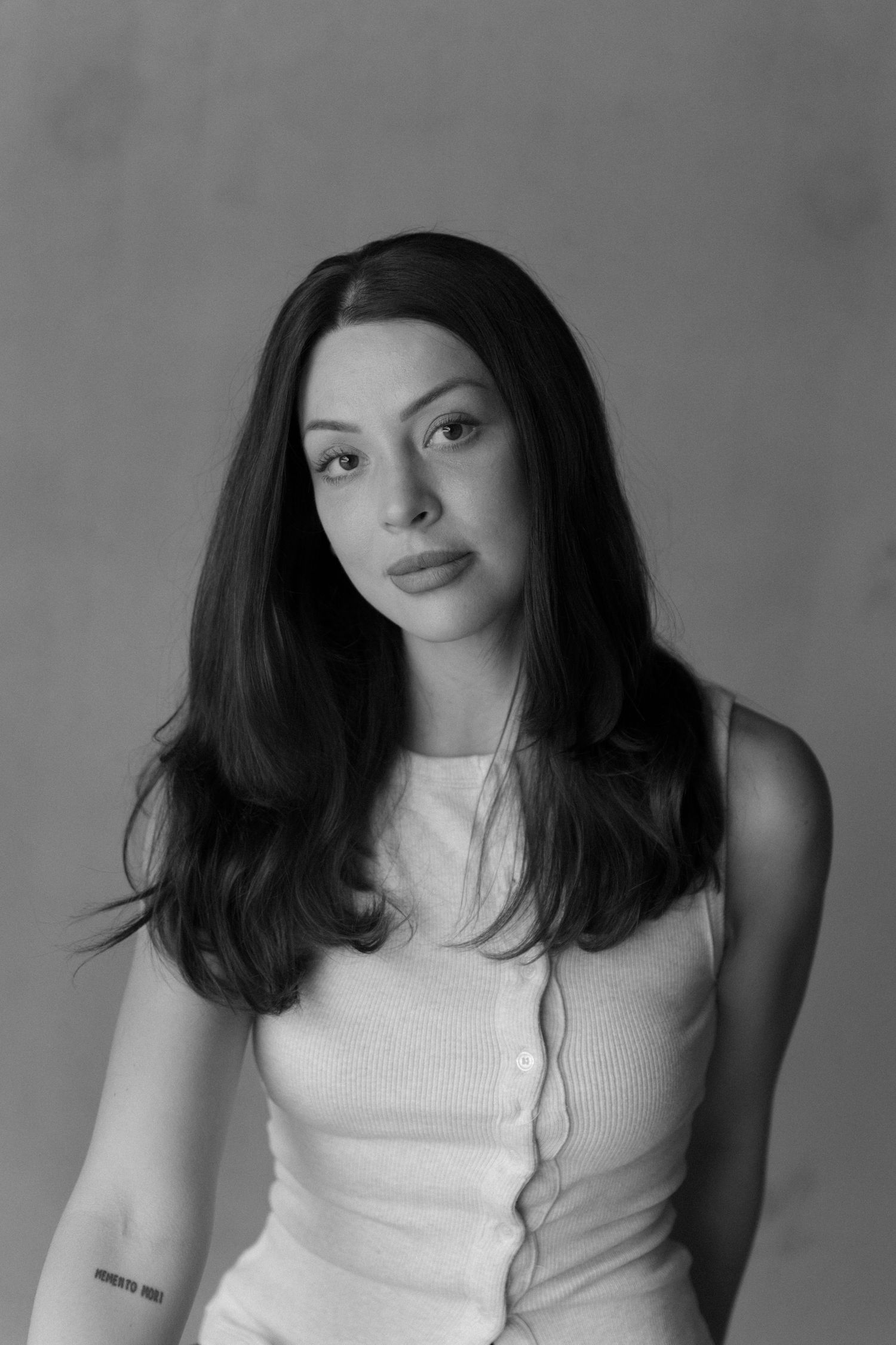 Black and white portrait showing dark-haired person in black clothing against neutral background.