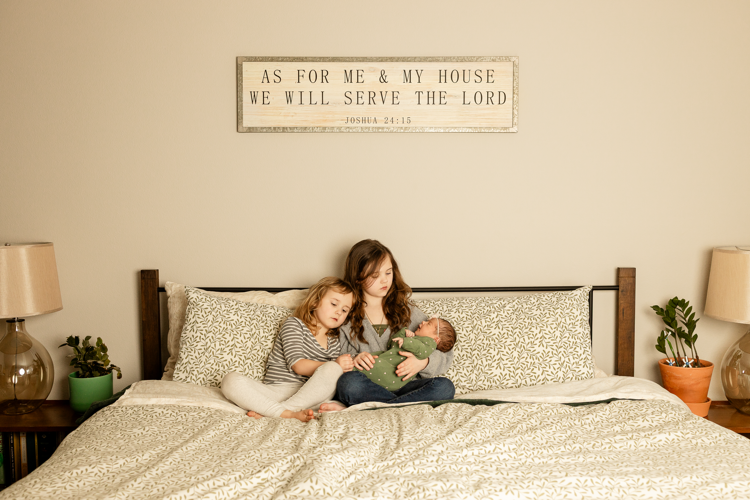 Two figures relaxing on a white bed with pillows under a sign reading 'As for me & my house'.