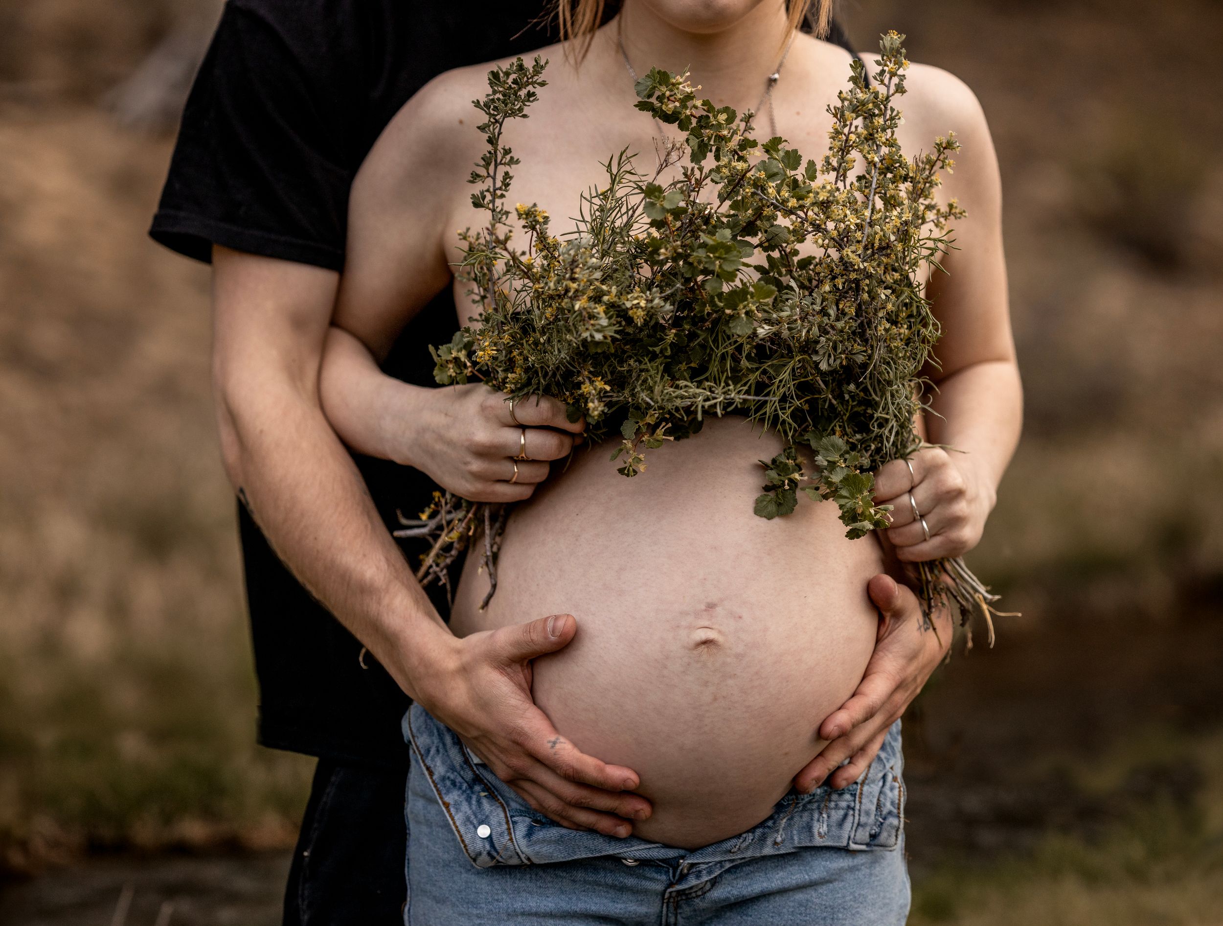Artistic maternity photo with fresh greenery held against pregnant belly.