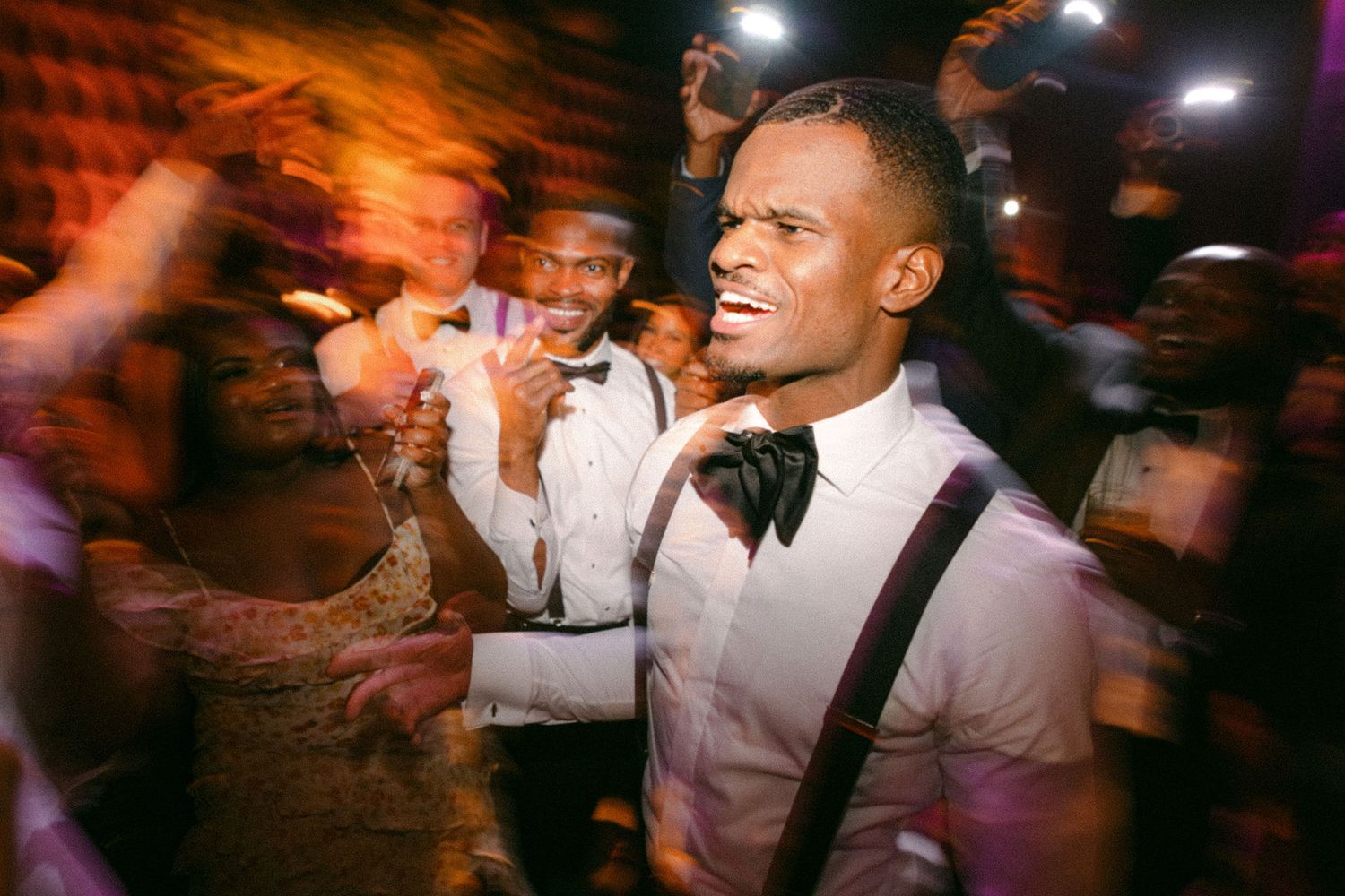 A festive party scene showing dancing guests in formal attire under colorful lighting.