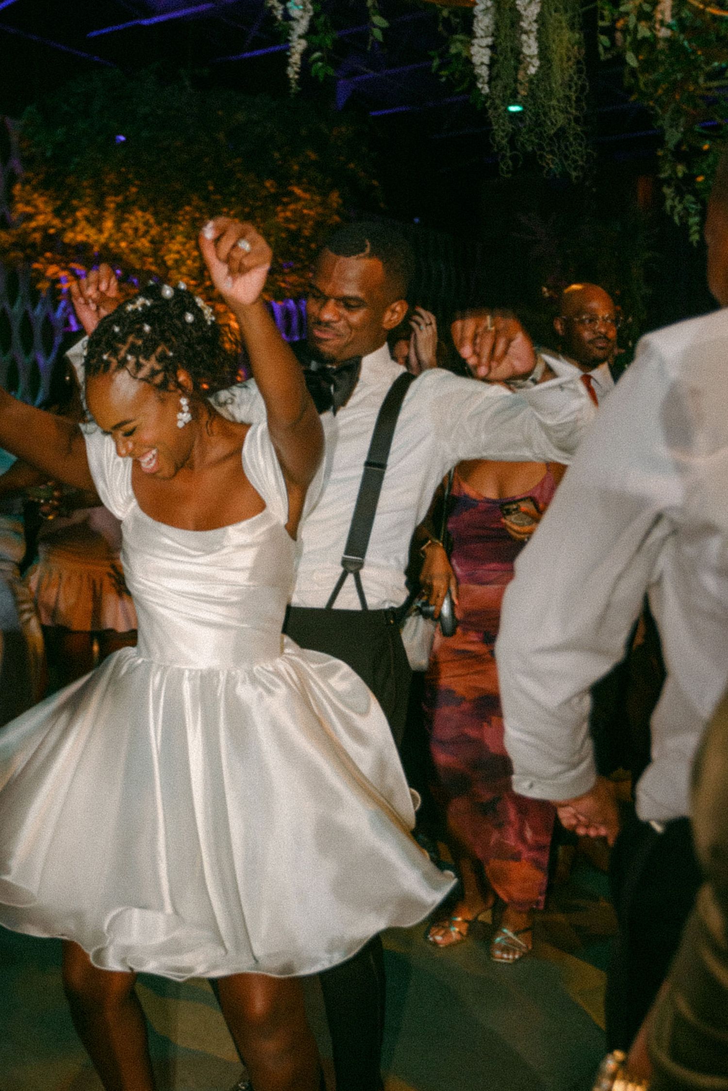 Wedding guests dancing enthusiastically under decorative hanging foliage.