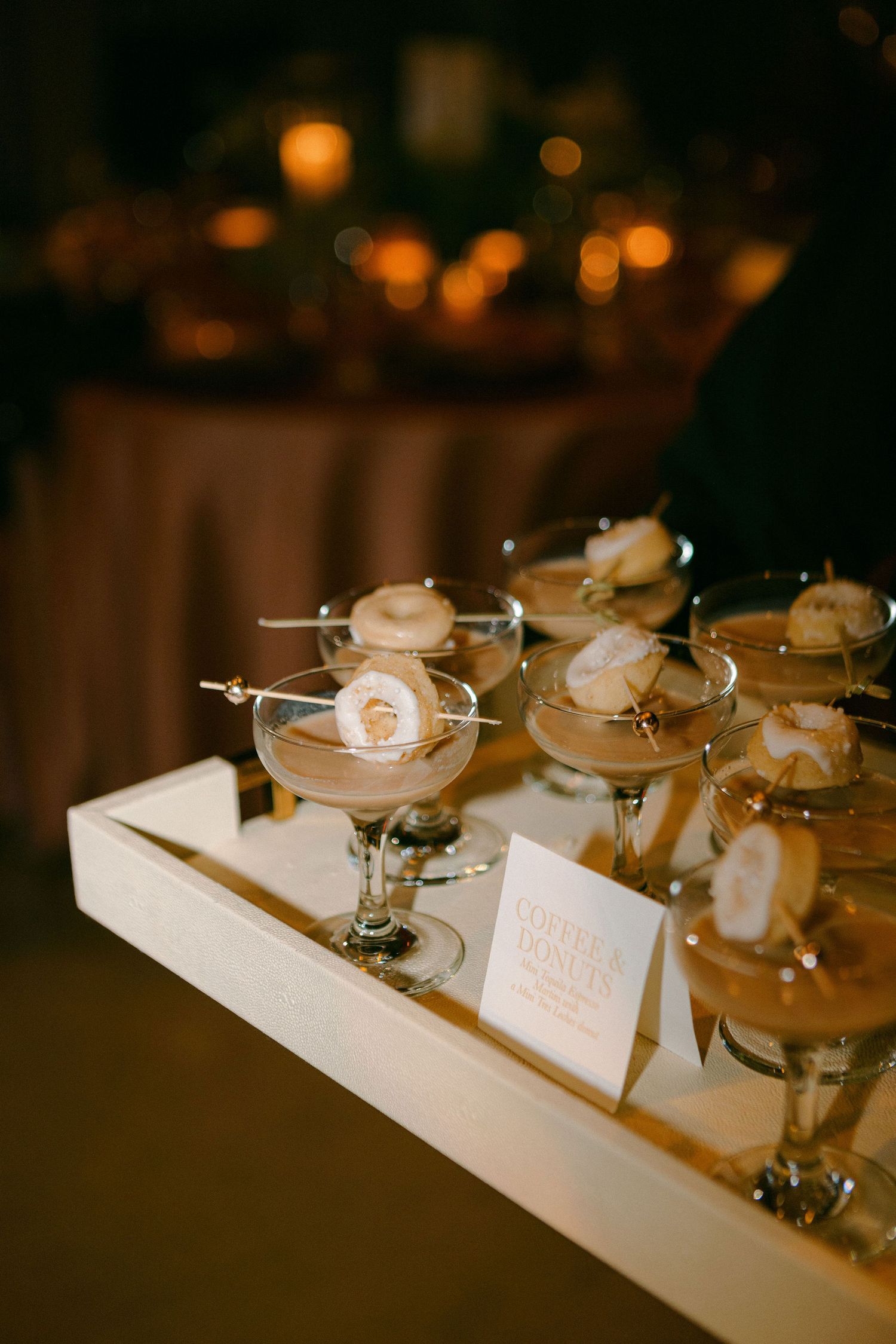 Elegant cocktails with white rose garnishes displayed on a serving tray at a wedding reception.