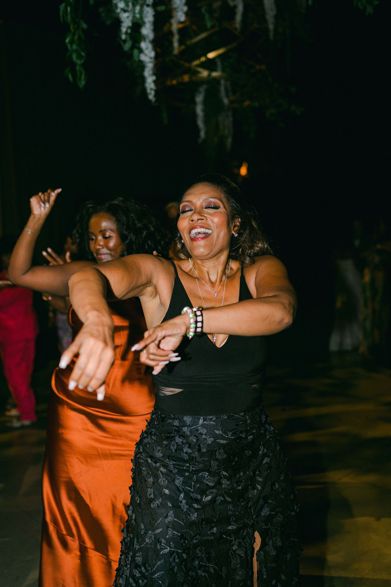 Two women dancing joyfully at a celebration in formal dresses.