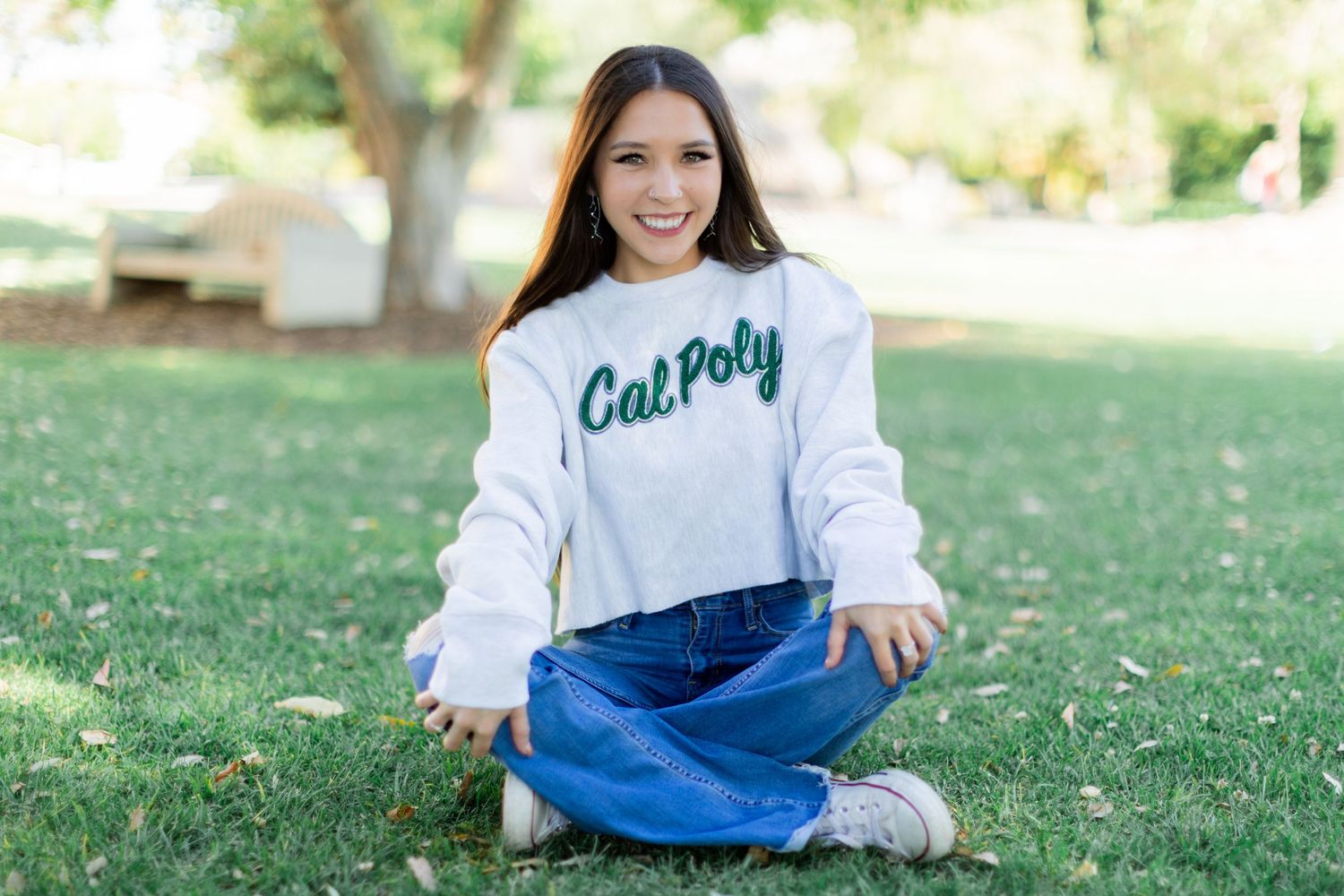 Senior session with a female in white sweatshirt relaxes on sunny grass lawn.