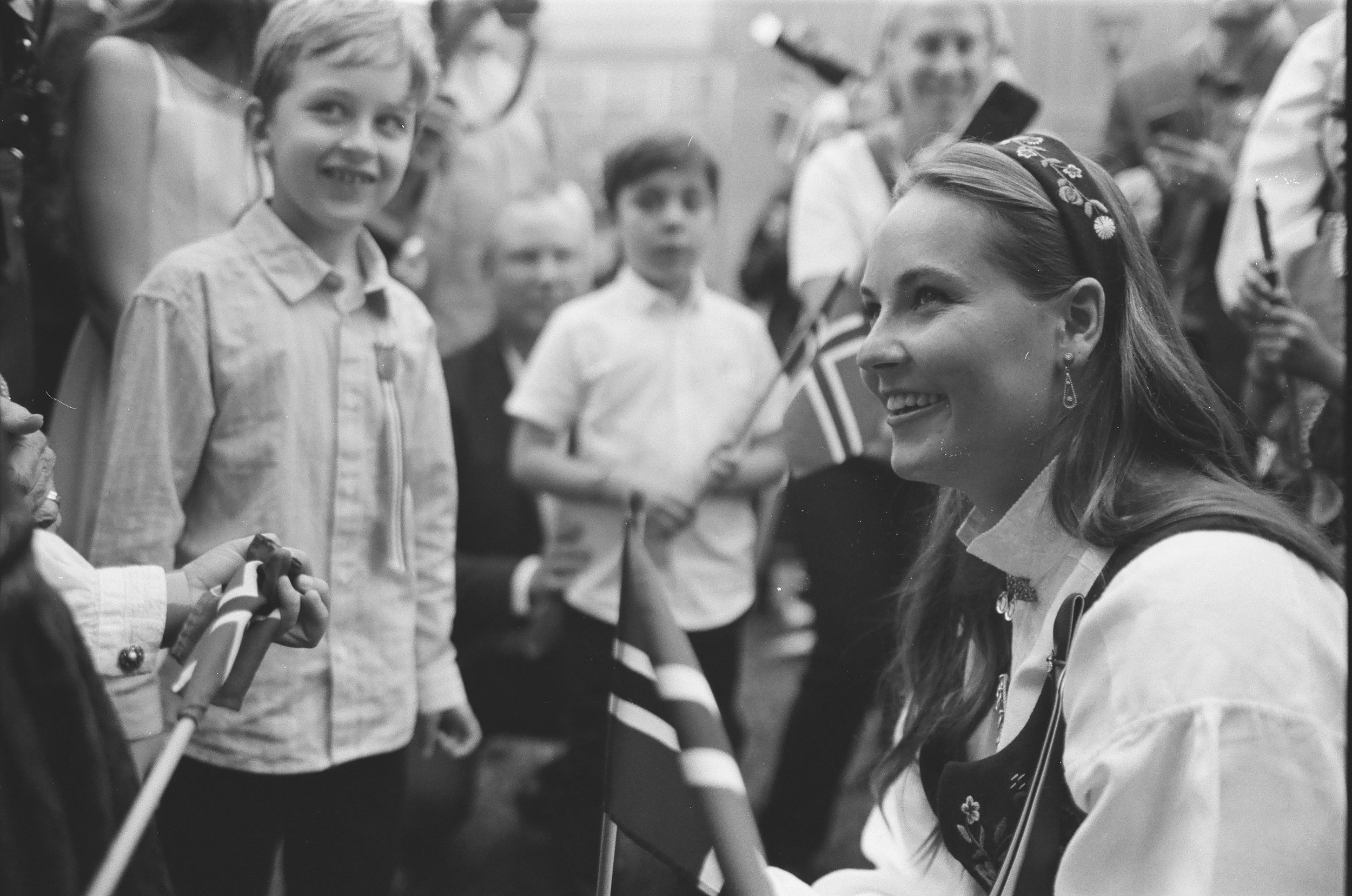 Black and white photo of a smiling woman in traditional dress with a young boy at a festive gathering.