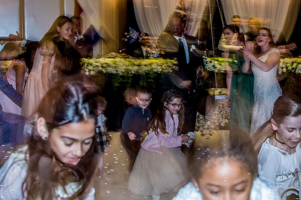 Guests dancing and celebrating at a festive wedding reception with decorative lighting.