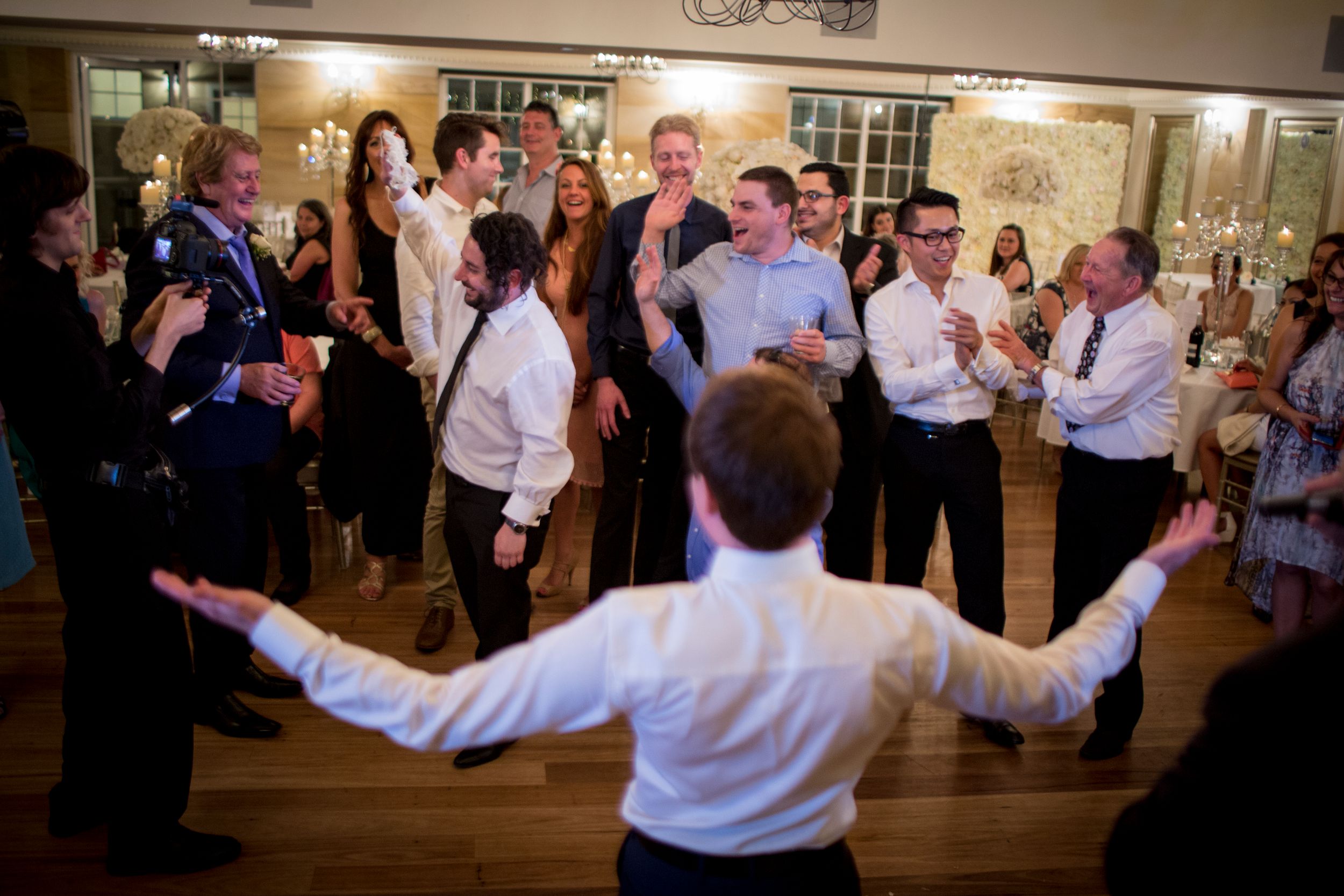 A lively dance celebration on a wooden floor at a reception event.