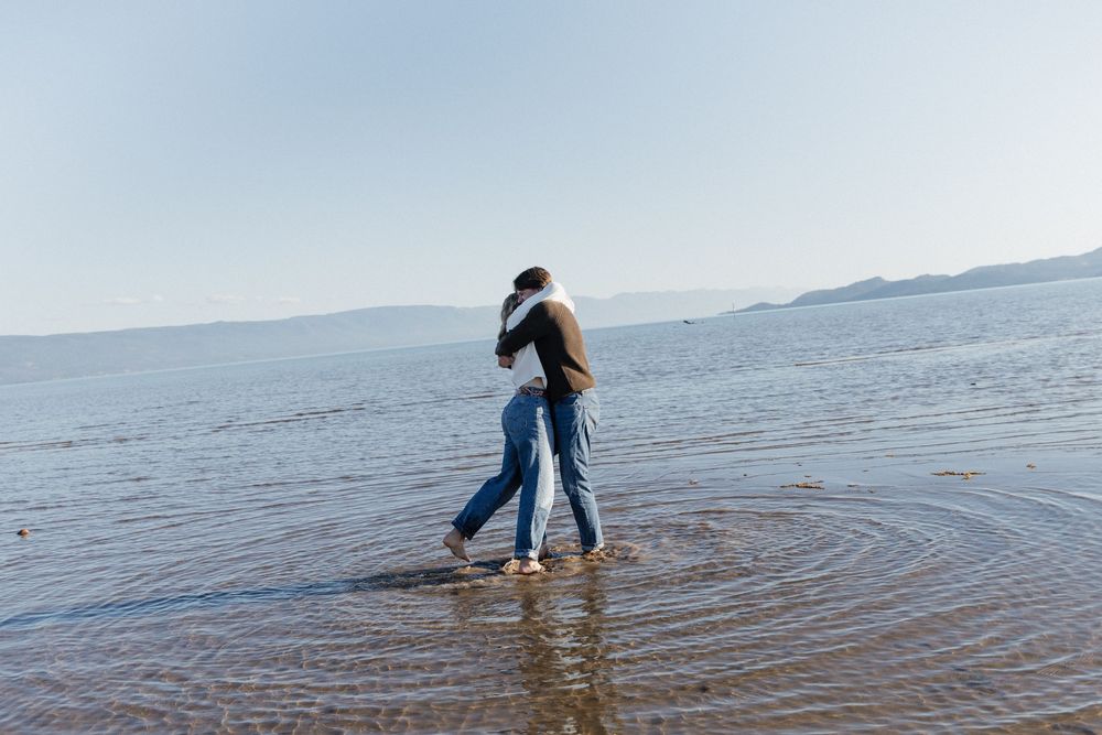 A person stands in shallow ocean water creating concentric ripples while the horizon stretches across the background.