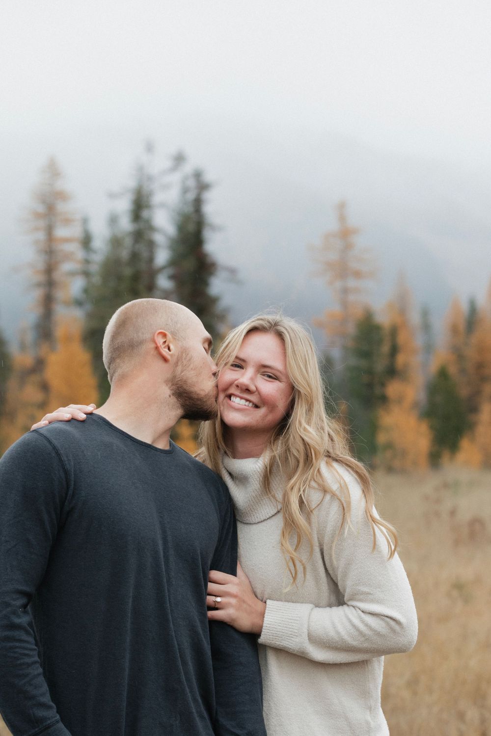 Romantic moment captured in autumn field with mountain backdrop.