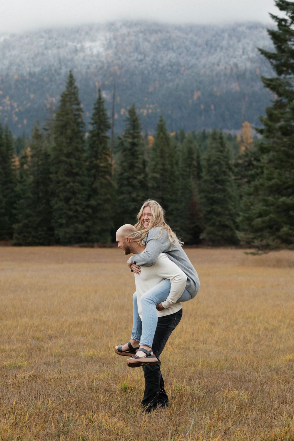 Playful piggyback ride in mountain meadow with forest backdrop.