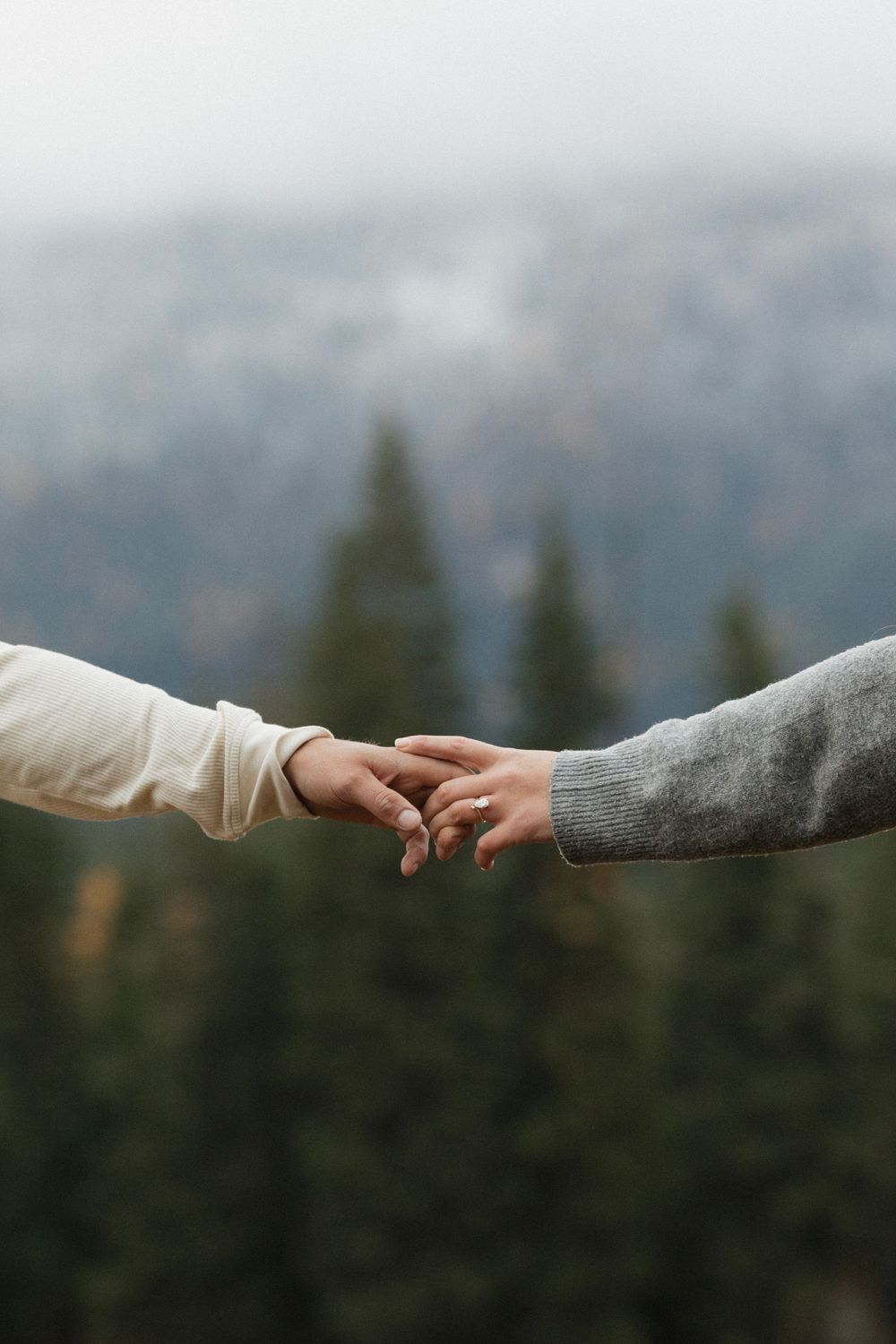 Two people holding hands tenderly against mountain forest backdrop.
