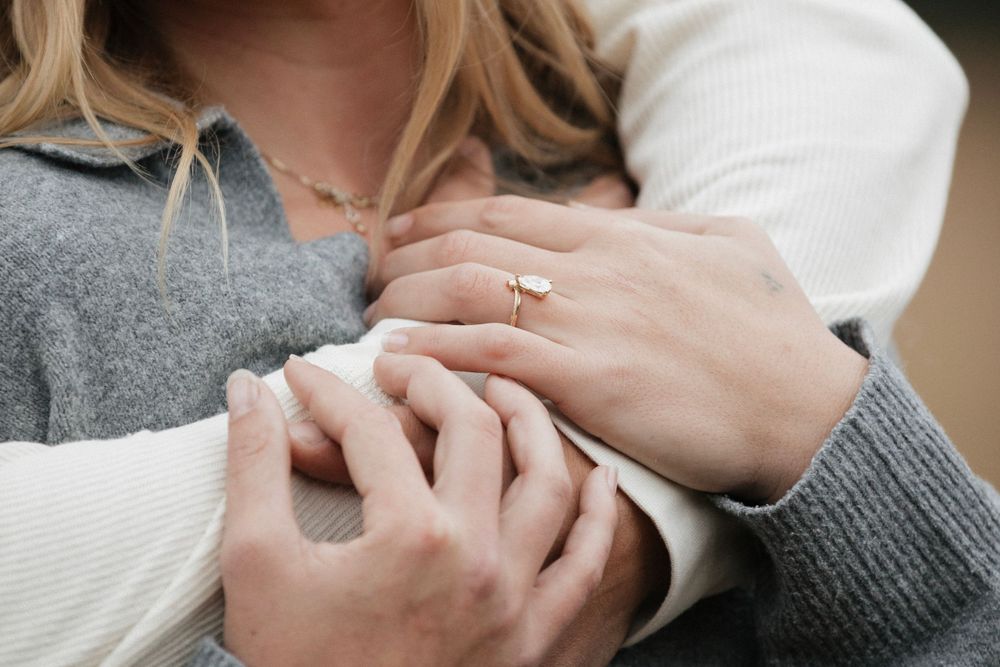 Close up detail shot of hands showing off an engagement ring against cozy sweaters.