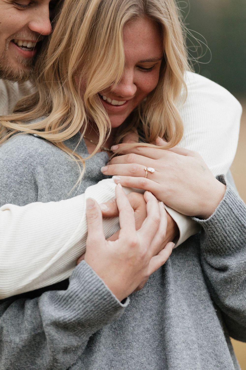 Intimate embrace showing hands wrapped around in warm sweaters against natural backdrop.