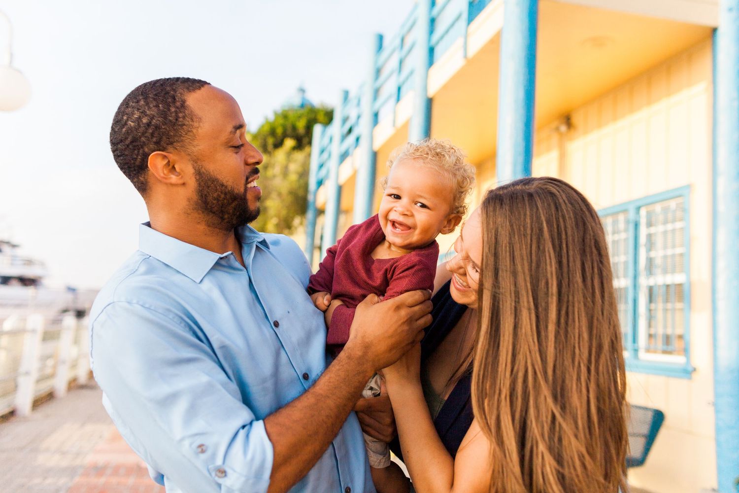 mom and dad holding toddler and looking at him while he smiles at the camera