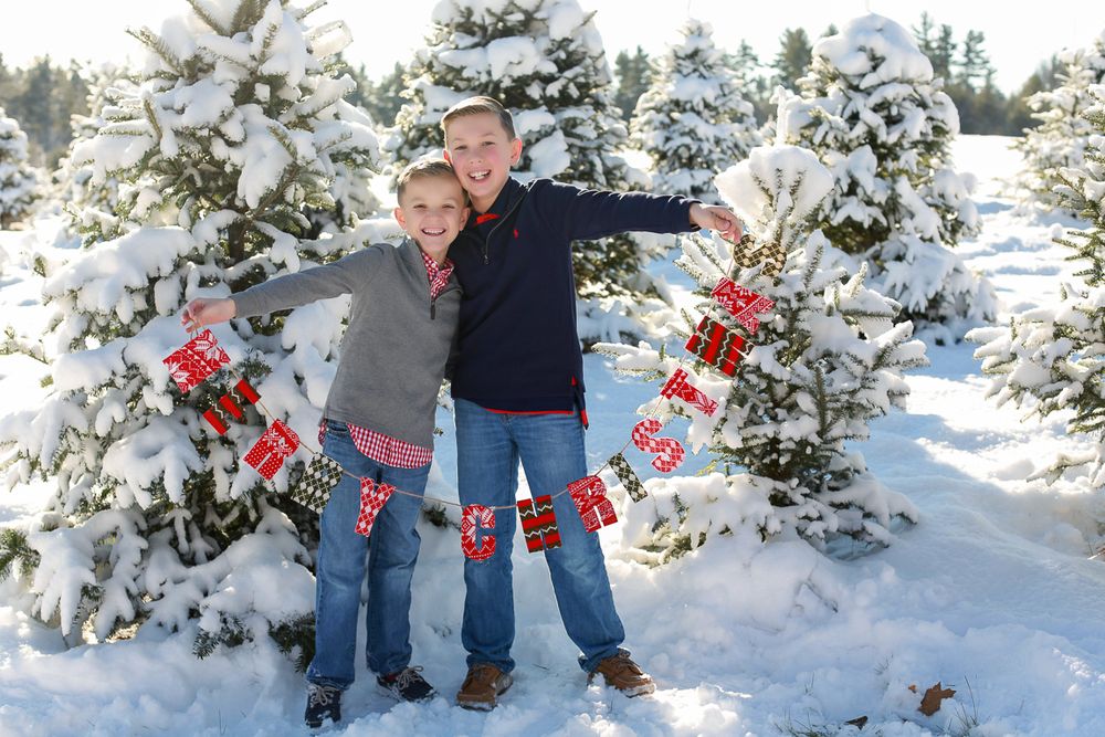 Tree farm covered in snow in Portsmouth New Hampshire family photographed holding merry Christmas sign