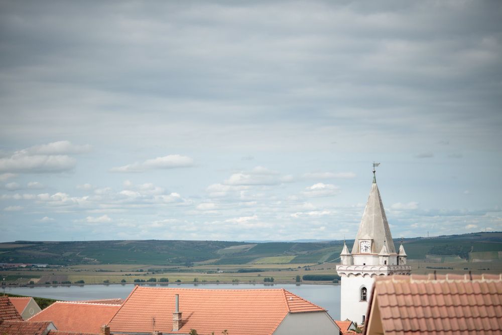 Church spire and red rooftops against cloudy sky in European town.