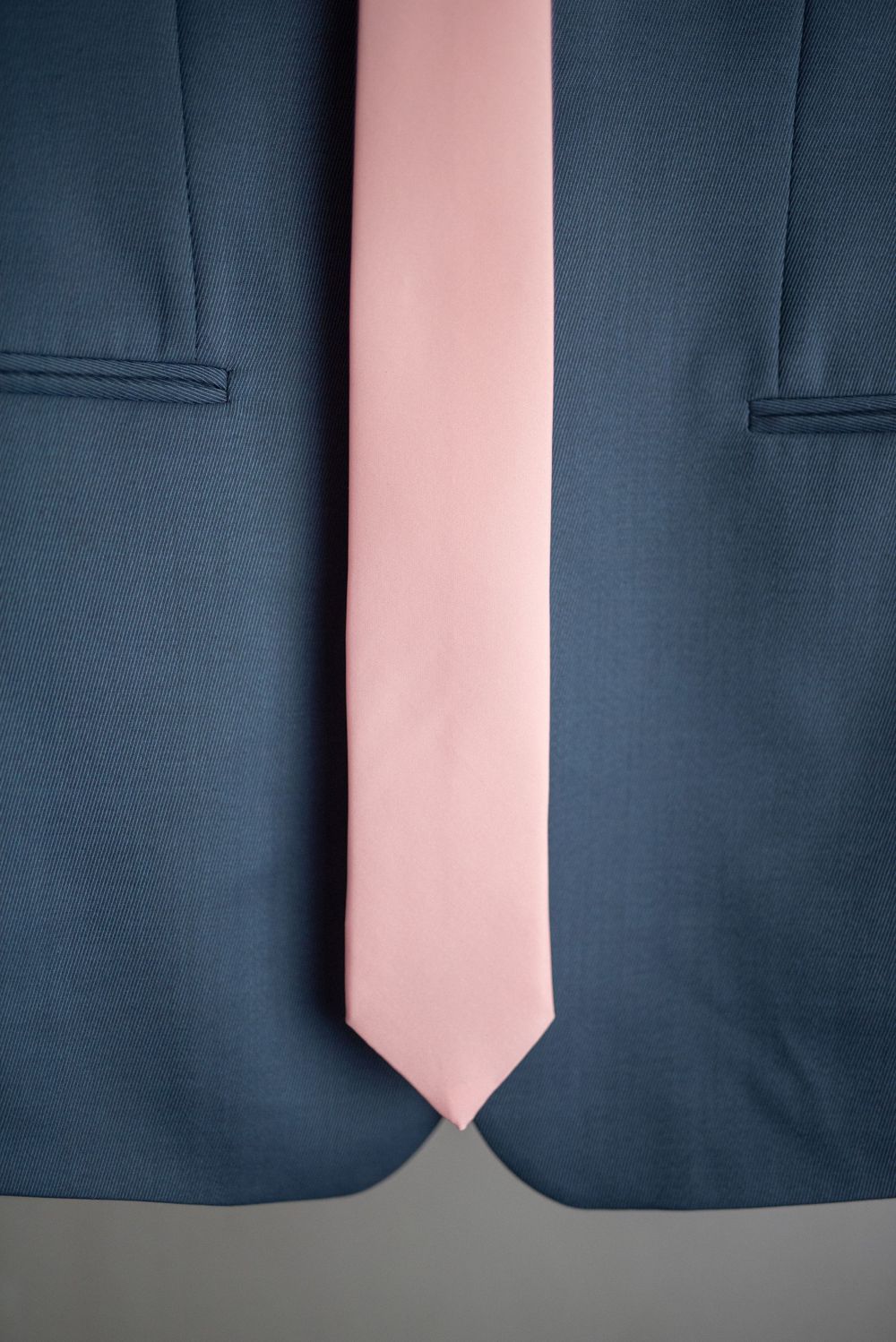 Pink tie laid over dark blue suit jacket showing texture and contrast.