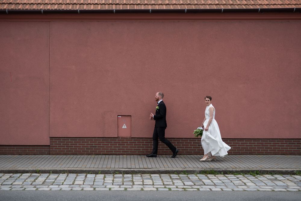 Wedding couple walking along red brick wall with cobblestone street.
