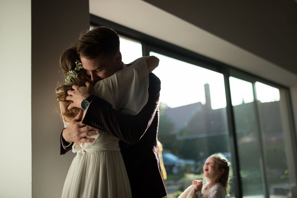 Romantic embrace in silhouette by sunlit window during wedding celebration.