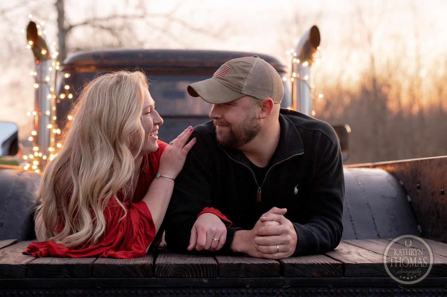A couple shares a playful moment in a truck bed decorated with string lights at dusk.