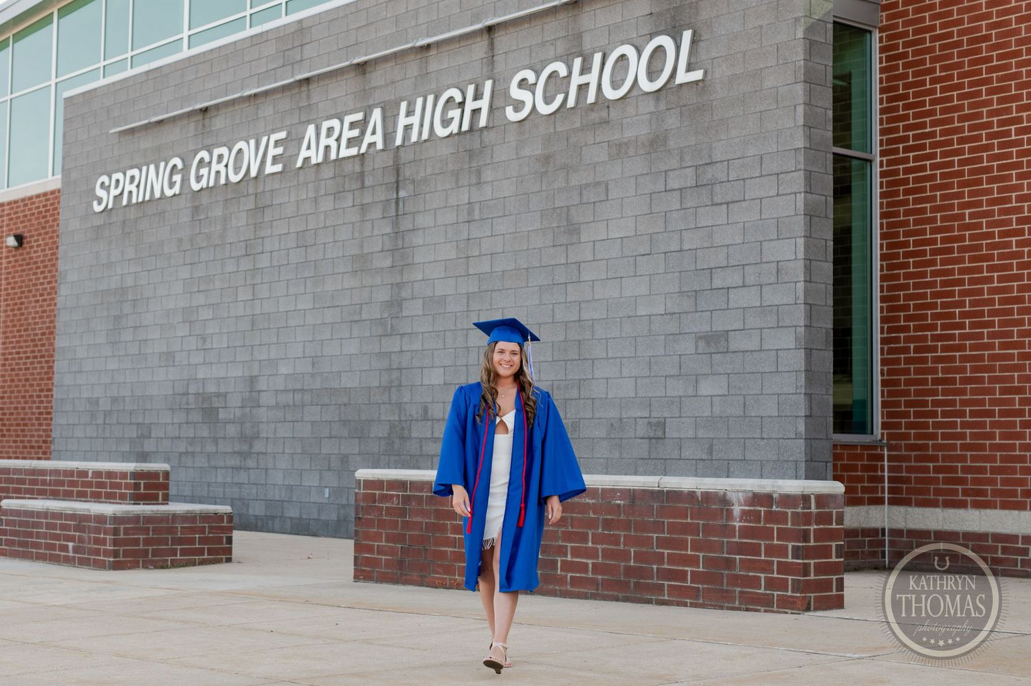 Graduate in blue cap and gown standing in front of Spring Grove Area High School entrance.