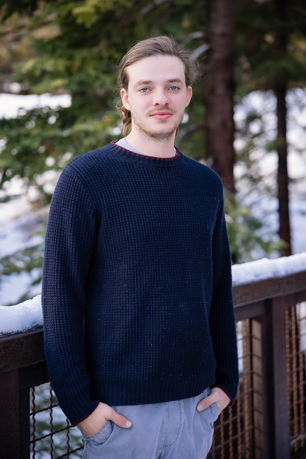 A young man poses outside with snow and trees in the background